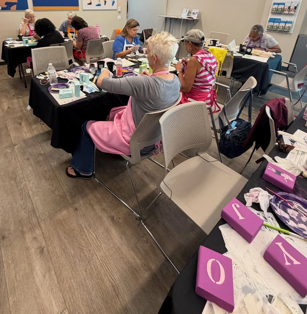 Group of women participating in a craft workshop around tables covered with supplies in a community center or classroom setting.