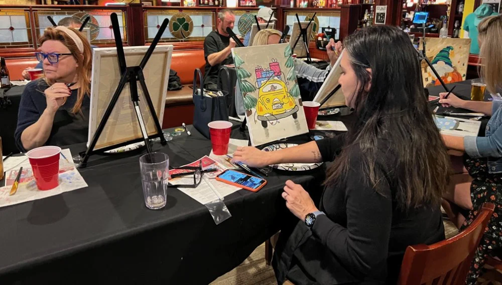 People painting colorful pictures on canvases at a group art class in a restaurant.