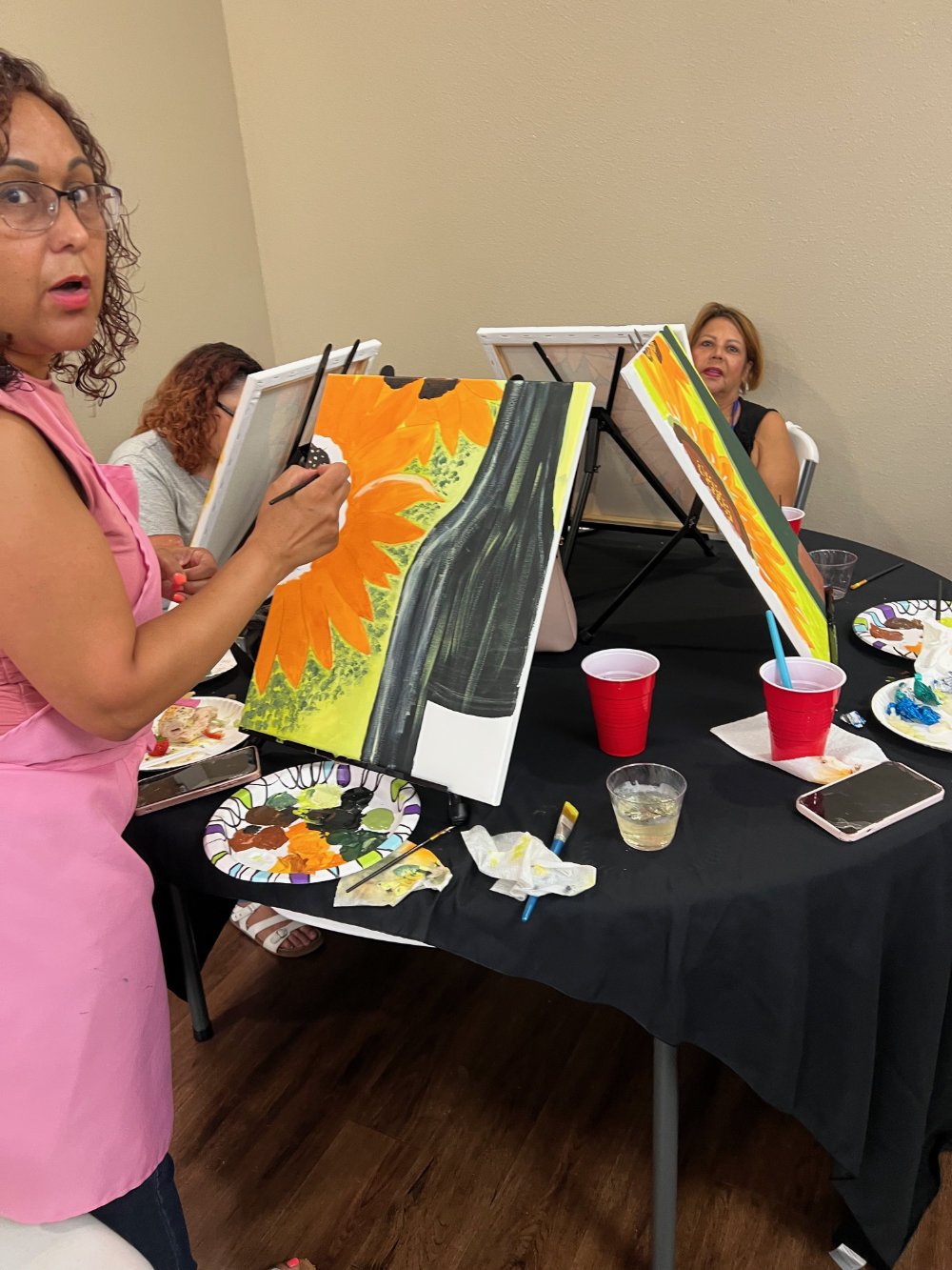Women painting sunflower-themed art on canvases during a group painting class.