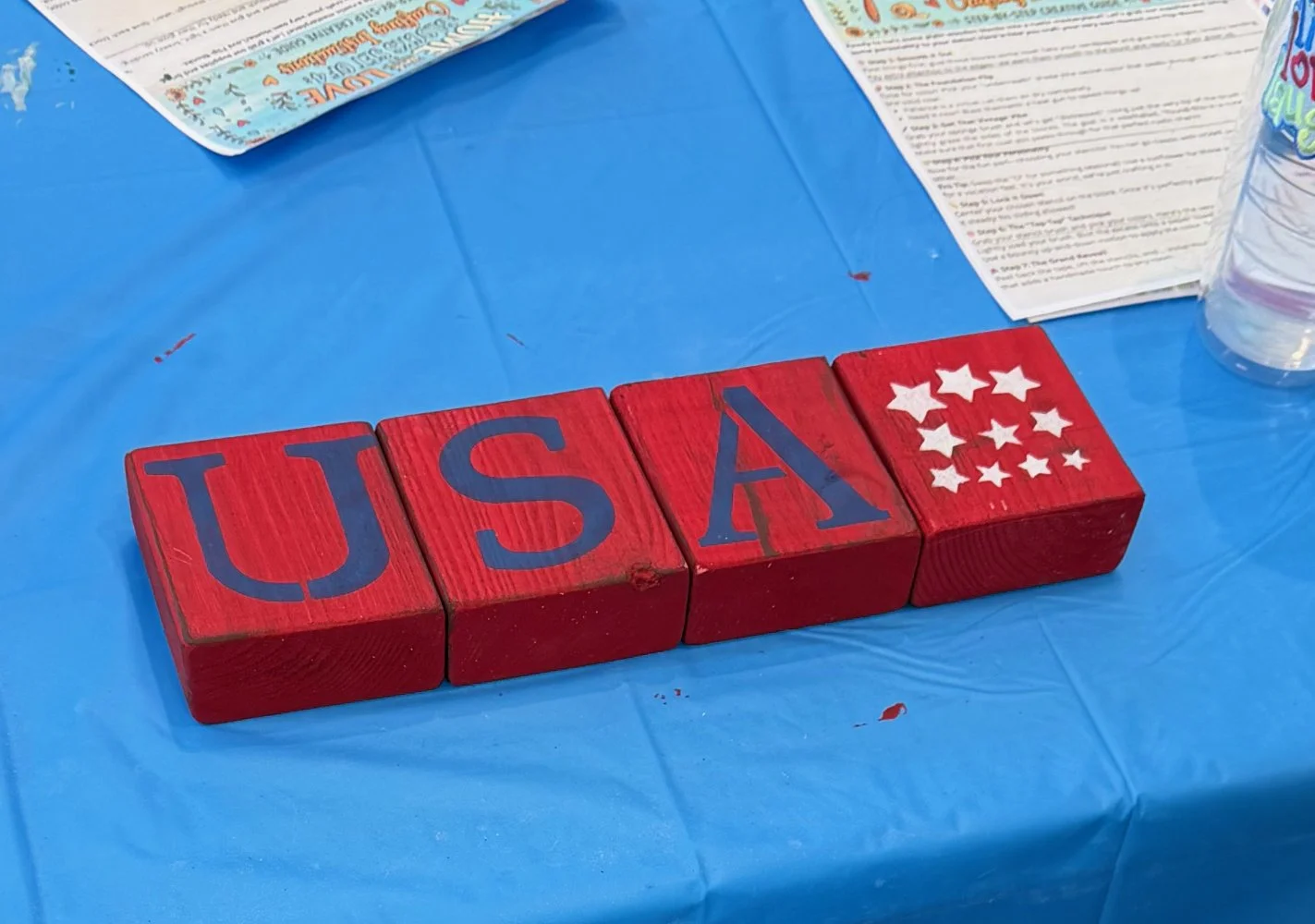 Red blocks spelling 'USA' with white stars, placed on a blue tablecloth at a celebration or event.
