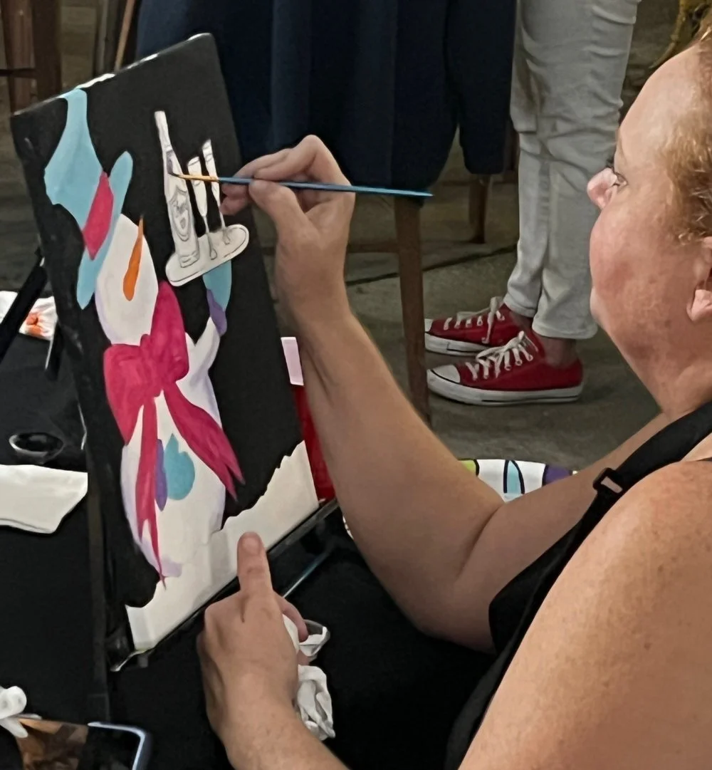 A woman painting a floral design on a black canvas with a paintbrush.