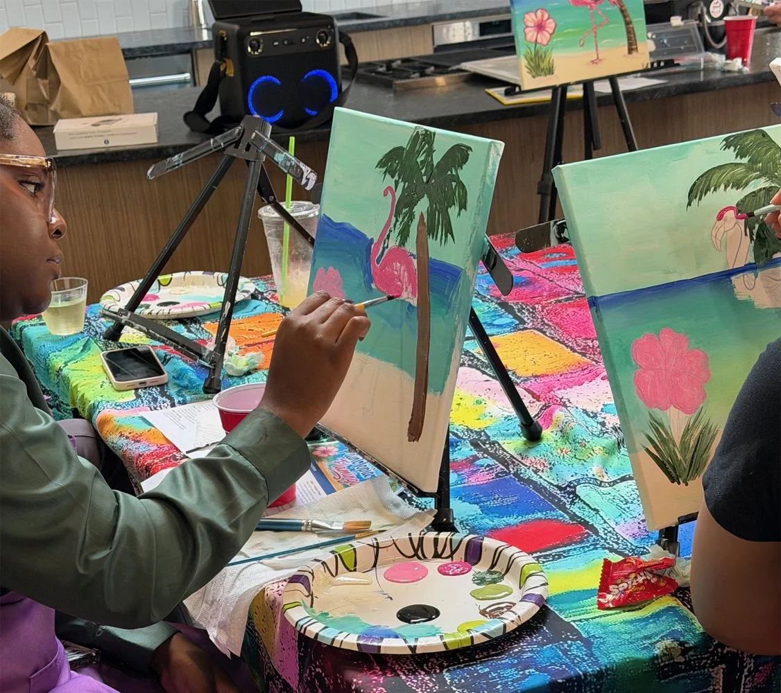 People painting pink flamingos on small canvases with tropical scenes in the background.
