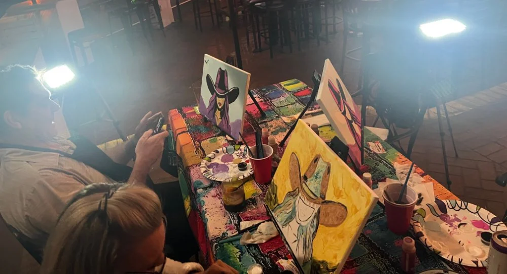 People painting colorful cowboy-themed artwork at a table covered with paint supplies.