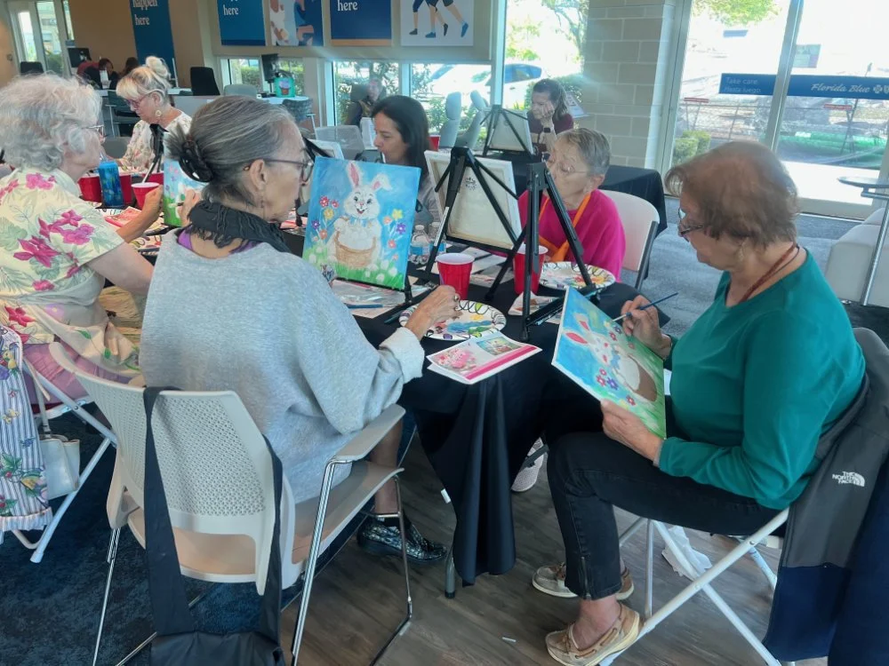 Group of elderly women participating in a painting class at a community center, painting pictures of bunnies and spring scenes.