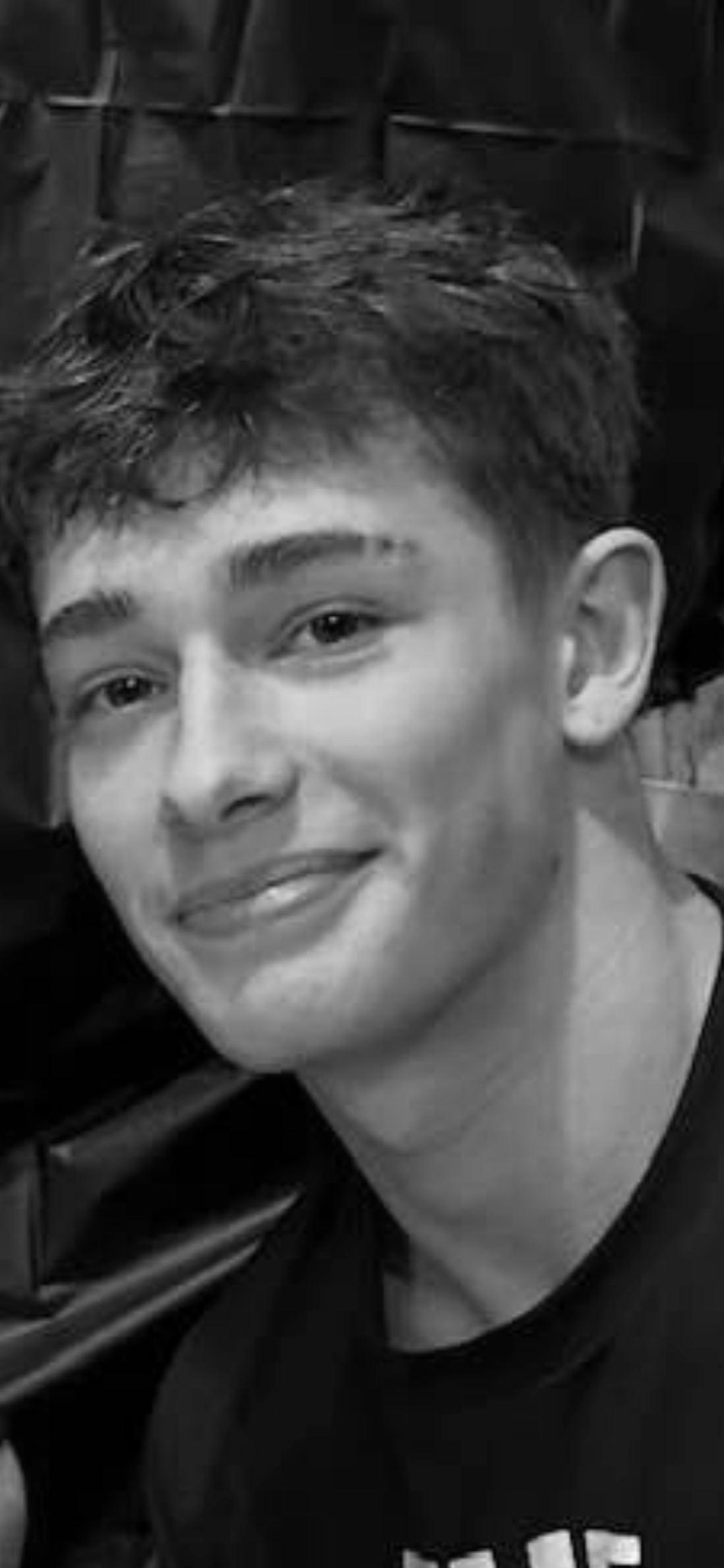 Black and white photo of a smiling young man with short, wavy hair, wearing a dark shirt.