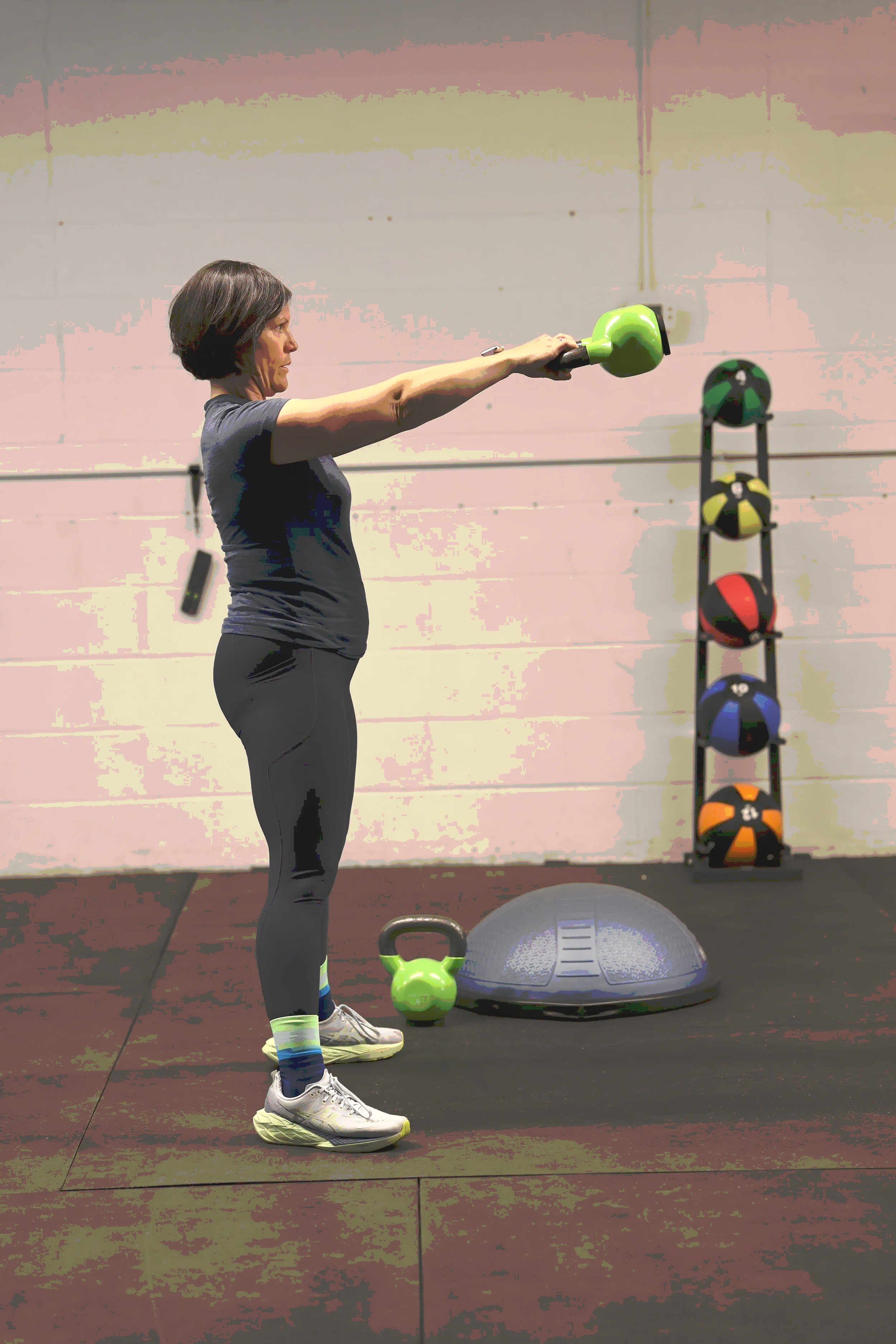Caroline Duncan performing a kettlebell exercise with a green kettlebell in a gym.