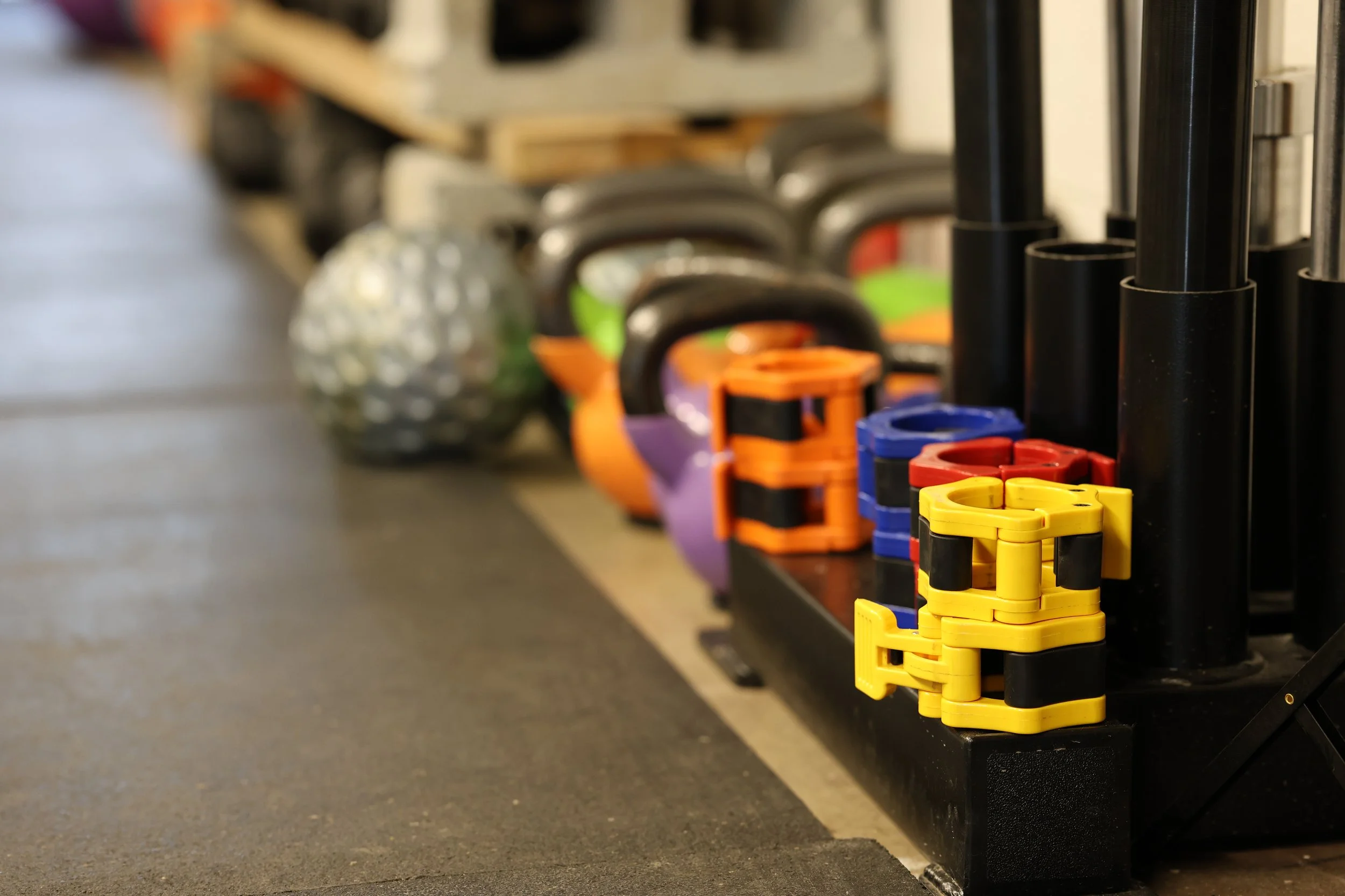 Colorful kettlebells arranged on a black rack in a gym.