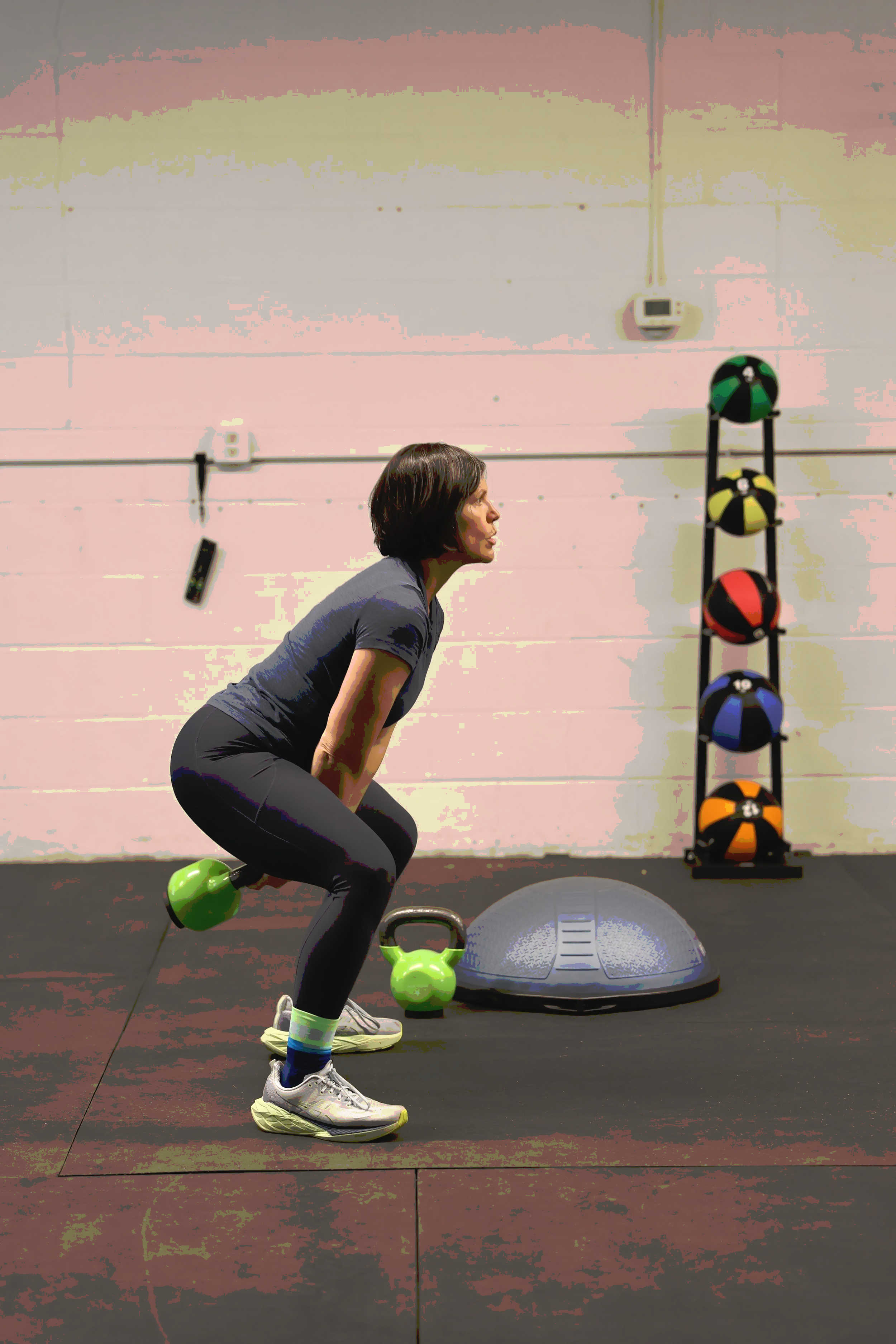 A woman performing a squat exercise with a green kettlebell in a gym.