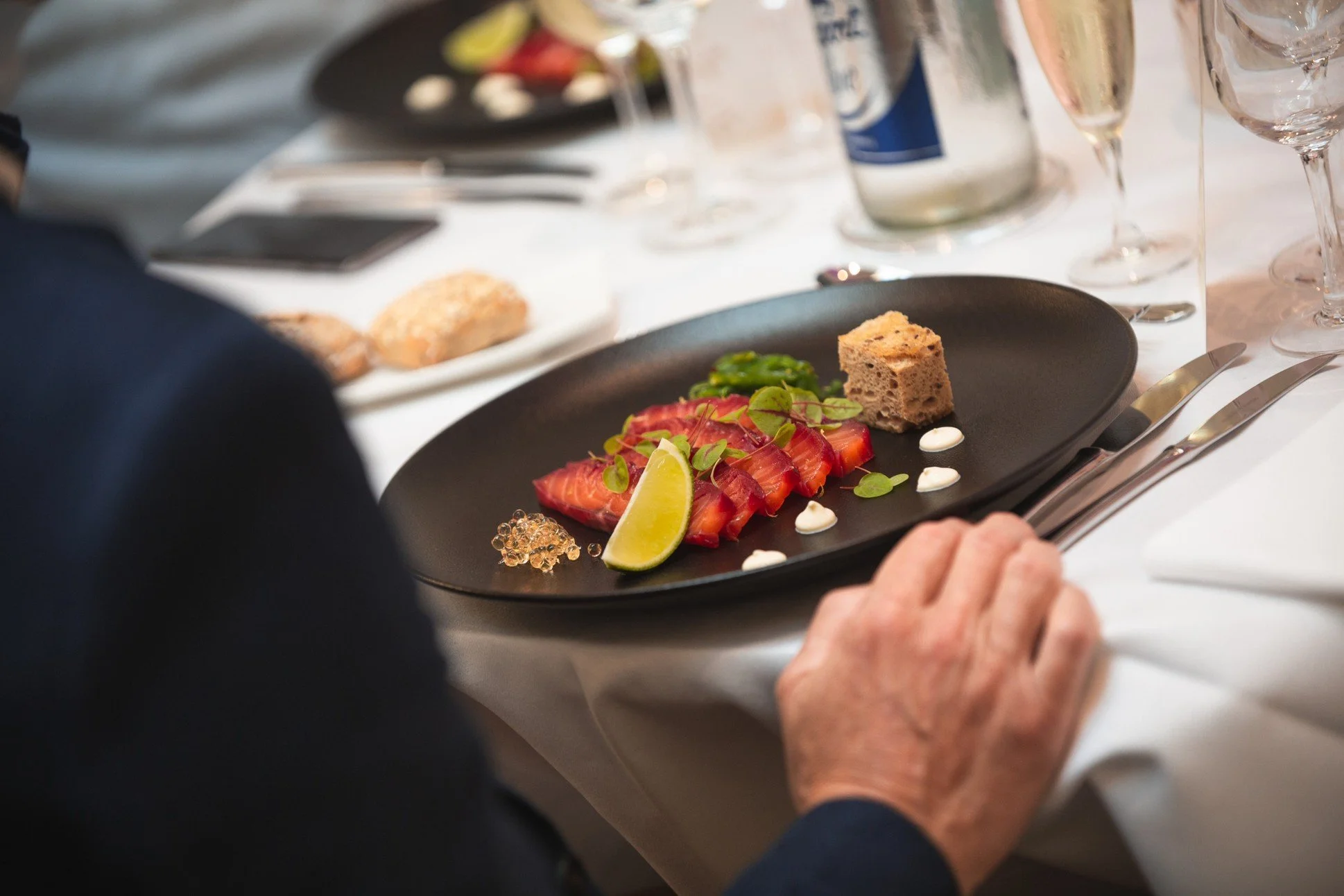 Assiette de fraises tranchées garnie de feuilles vertes, d'une tranche de citron vert et de petits cubes de pain ou de gâteau, accompagnée de petites cuillères et de verreries à champagne sur une table de dîner.