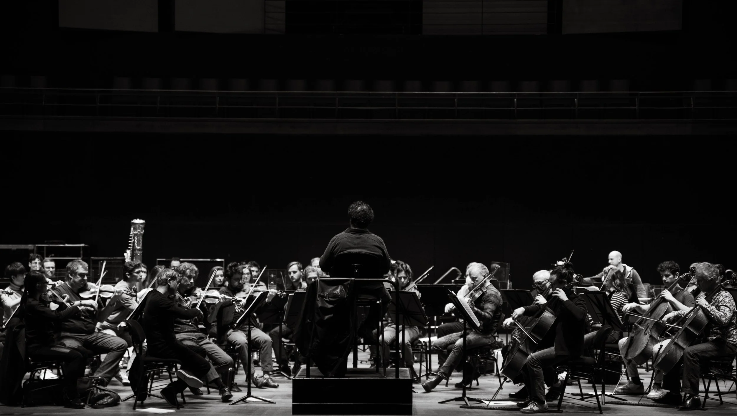 Orchestre symphonique en répétition dirigé par un chef d'orchestre, scène en noir et blanc.