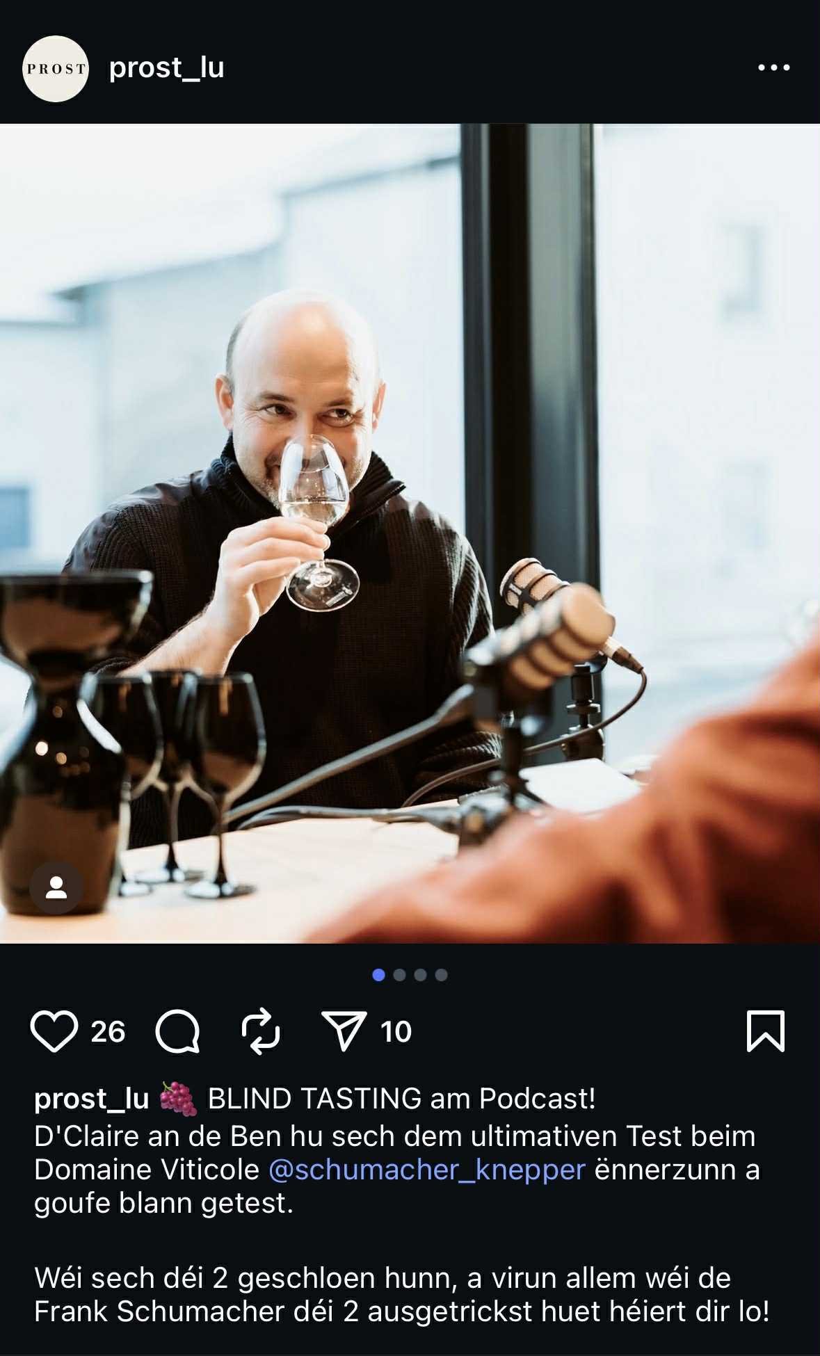 Un homme à la tête rasée tenant un verre de vin blanc devant un micro, dans une ambiance de dégustation ou podcast.