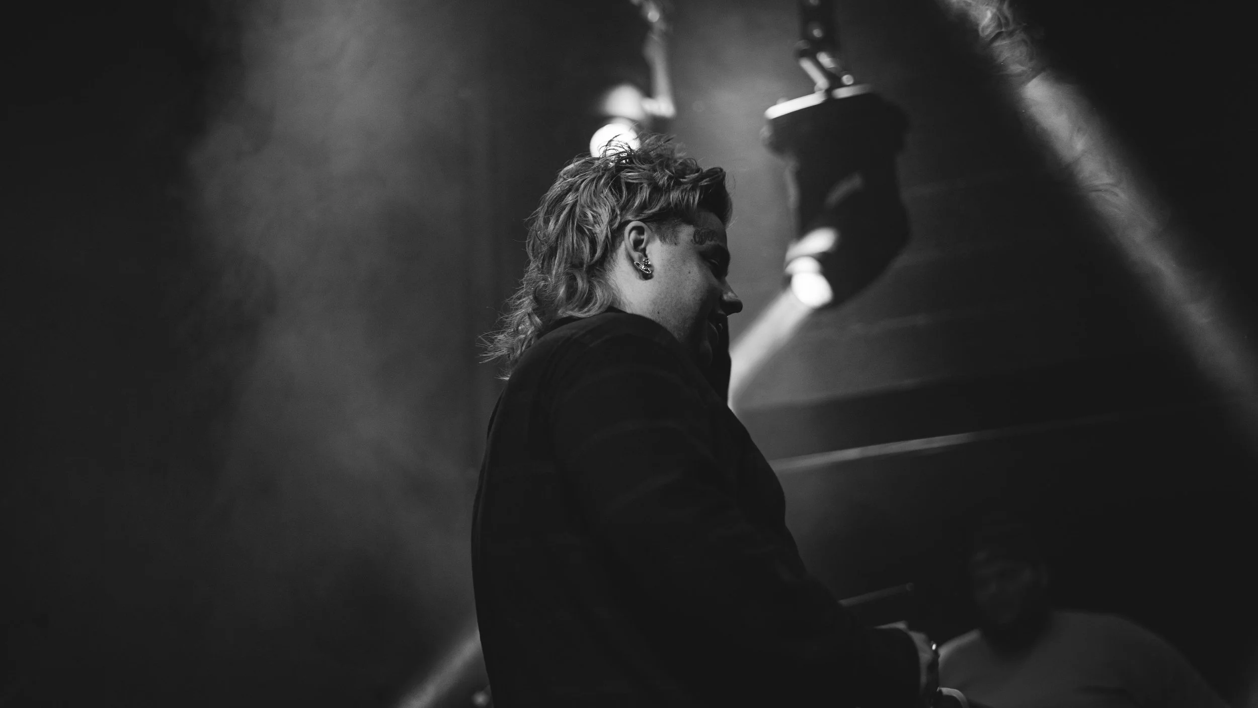 Une personne jouant du piano, vue de profil, dans une ambiance sombre et brumeuse, en noir et blanc.