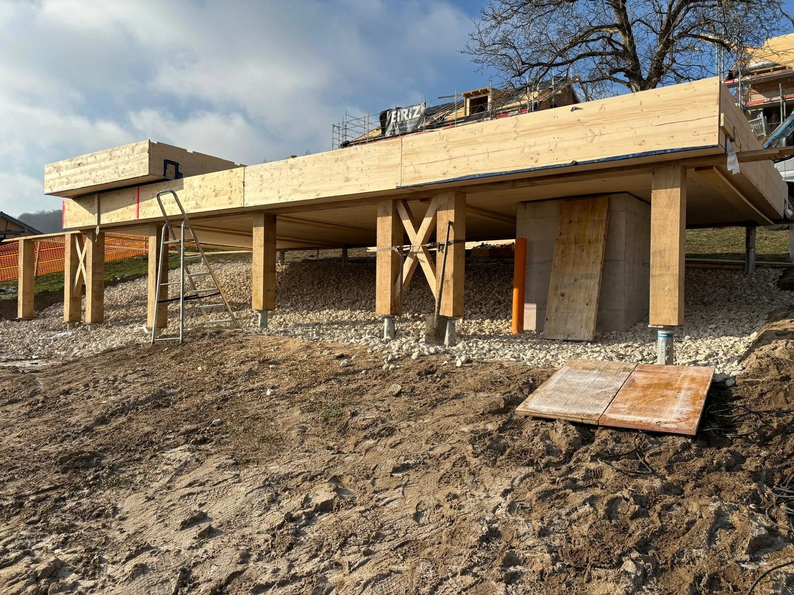 Construction d'une terrasse en bois sur pilotis, avec feuilles de bois et échelle sur terrain en terre.