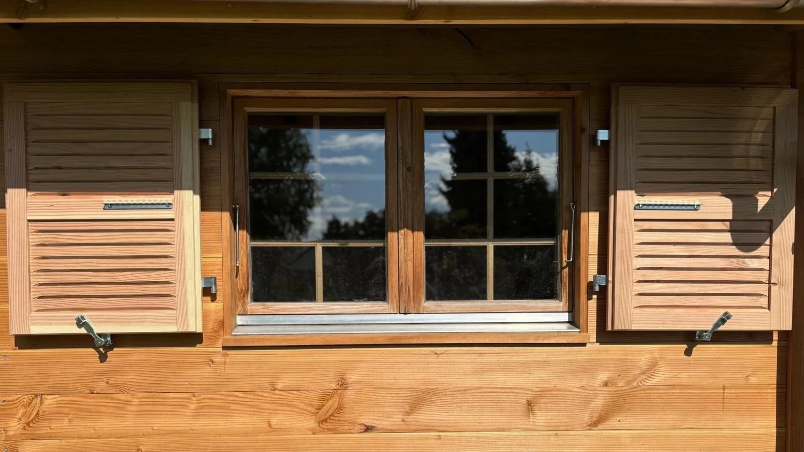 Fenêtre en bois avec volets et reflet d'un ciel bleu avec nuages. Volet en Persienne. 