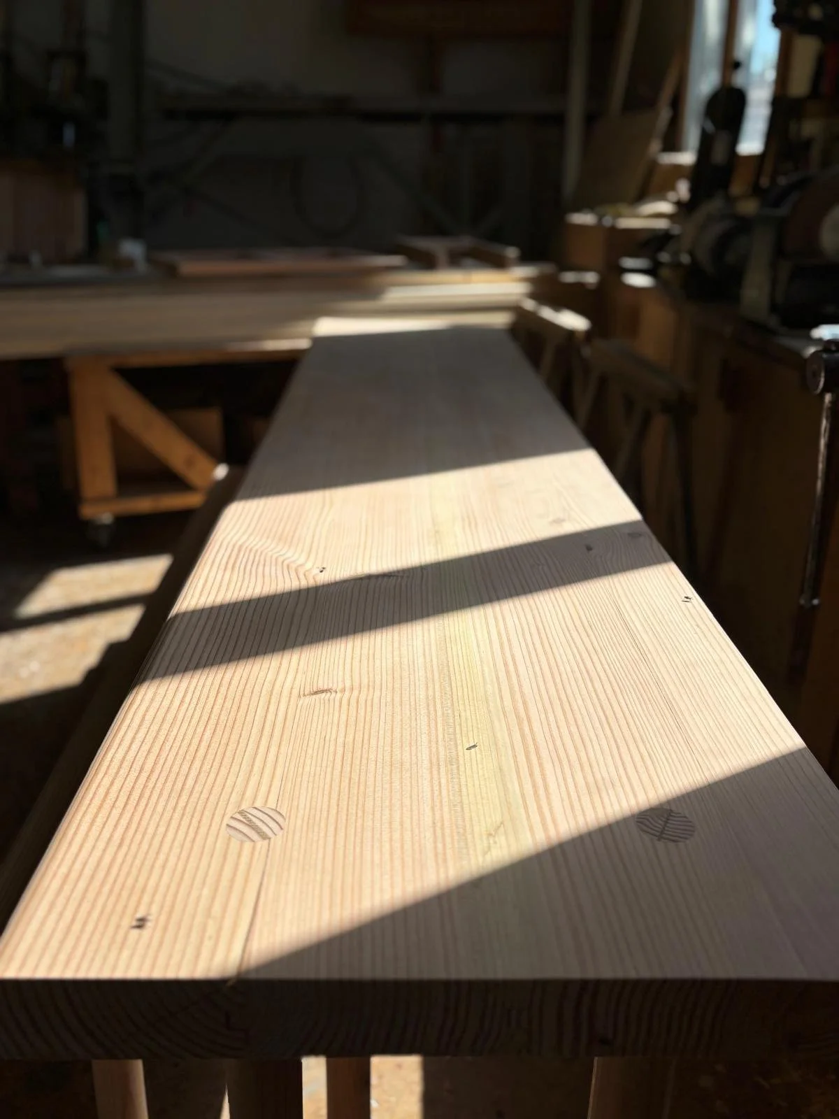 Planche en bois dans un atelier de menuiserie, avec des rayons de lumière passant à travers une fenêtre et créant des ombres sur la surface. Banc, menuiserie. 