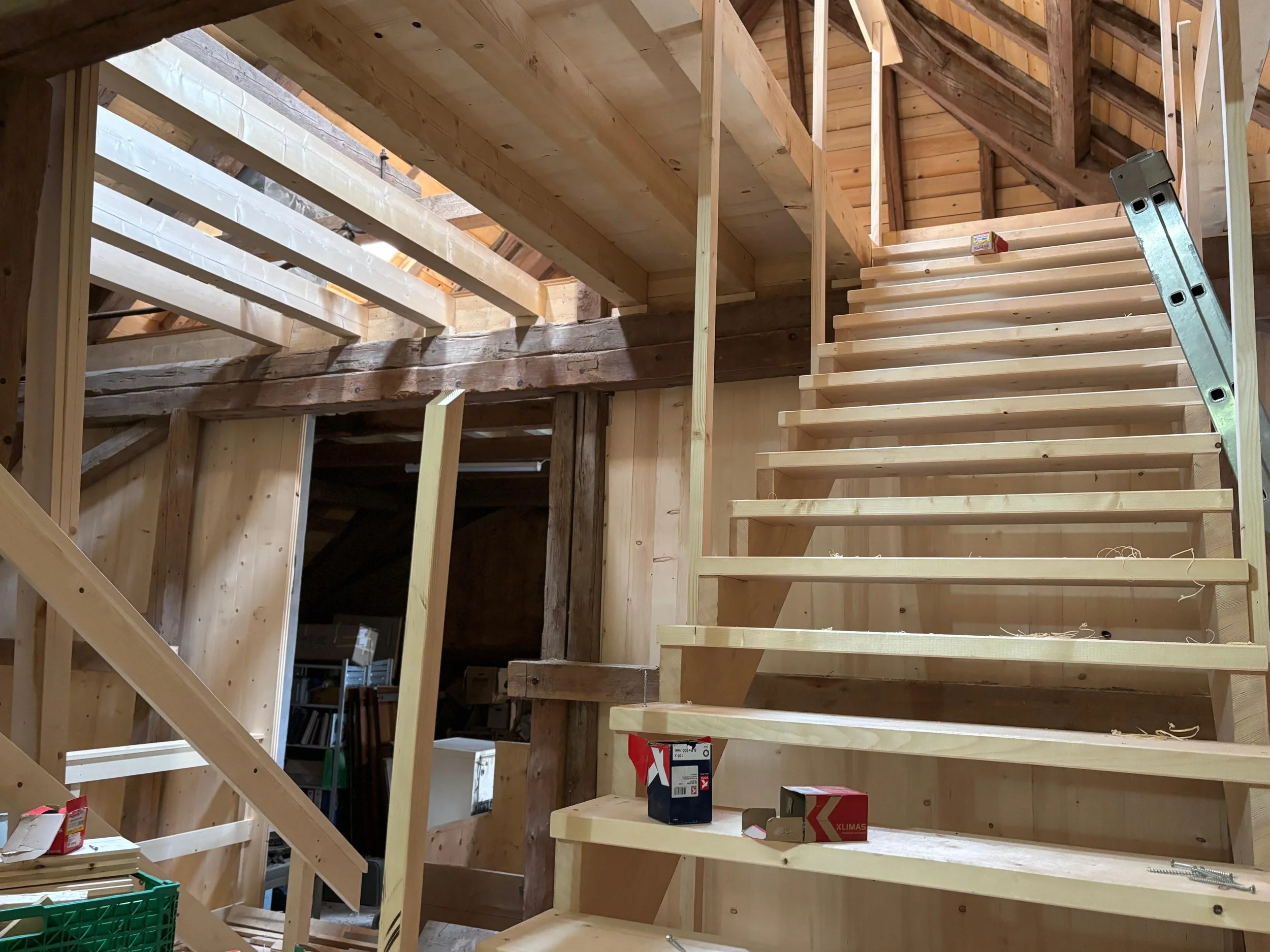 Intérieur en cours de construction d'une maison en bois, avec escalier en bois, poutres apparentes et espace en travaux.