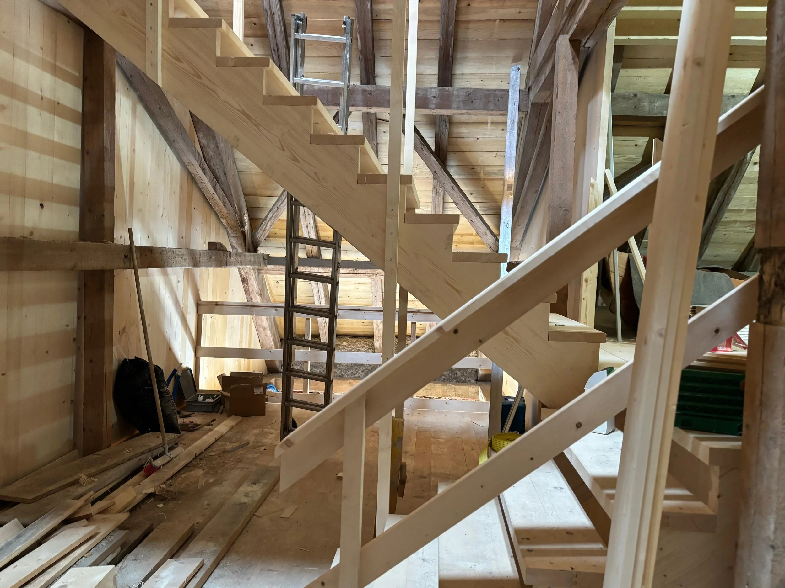 Une mezzanine en cours de construction dans une pièce en bois, avec des escaliers en bois partiellement installés, des outils et matériaux de construction autour.Renovation Ancienne grange en Séchoir à plantes 