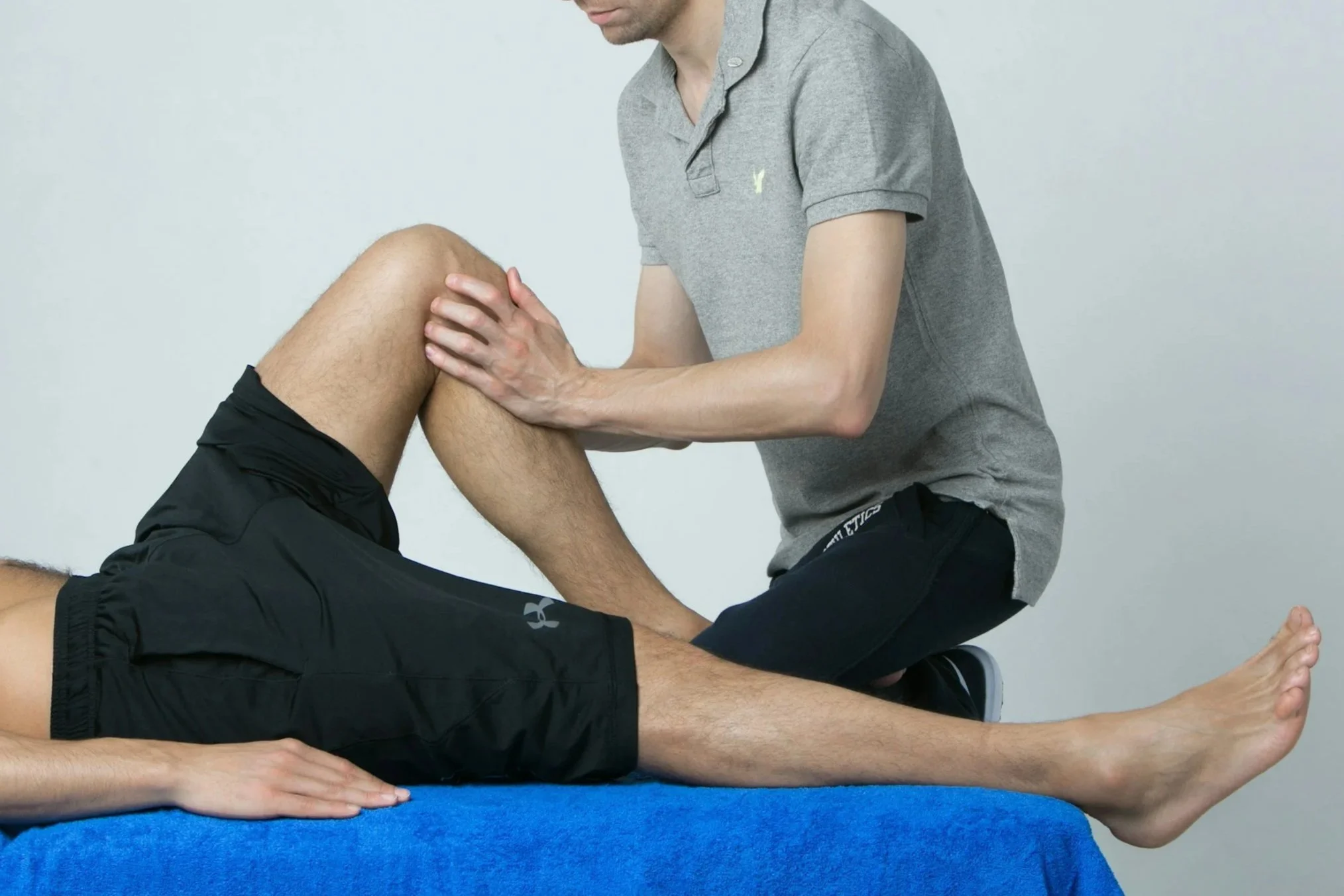 A person receiving physical therapy or a medical examination on their knee, lying on a treatment table while a therapist supports their leg.
