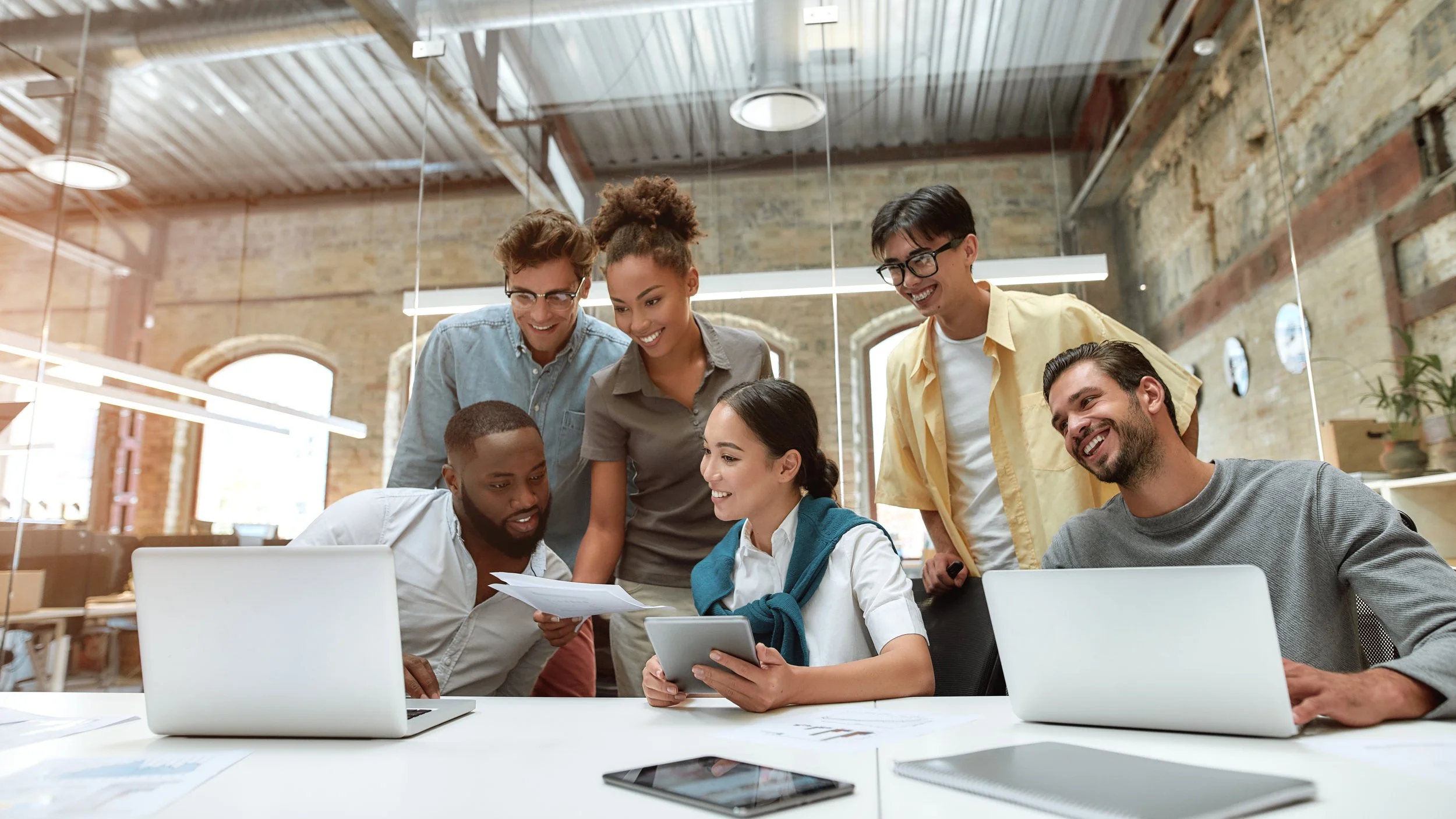 Group of diverse young professionals collaborating around a laptop and tablet in a modern office.