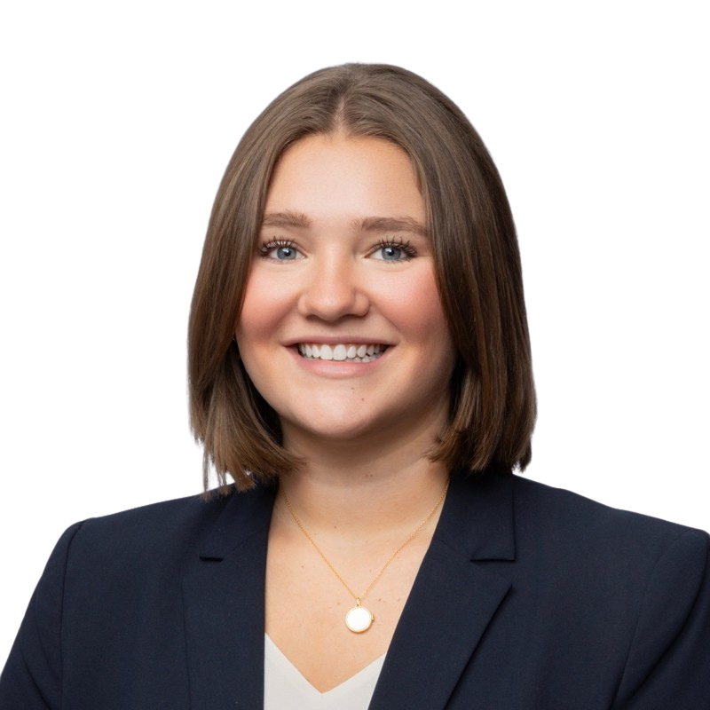 A young woman with shoulder-length brown hair, smiling, wearing a black blazer over a white top, and a gold necklace, against a plain white background.