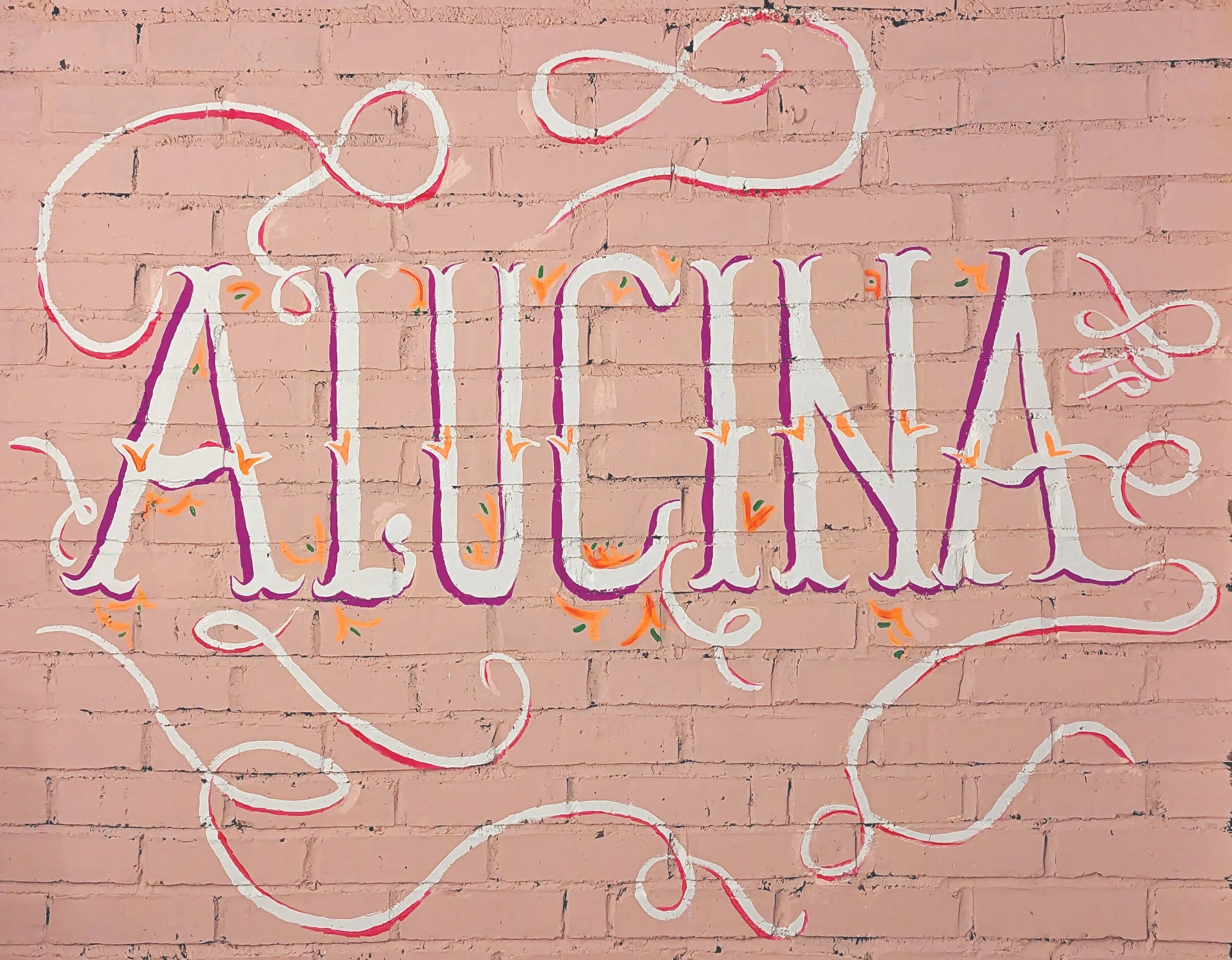 Decorative wall art with the phrase 'Arriving August' painted on a pink brick wall, featuring colorful swirls and accents.