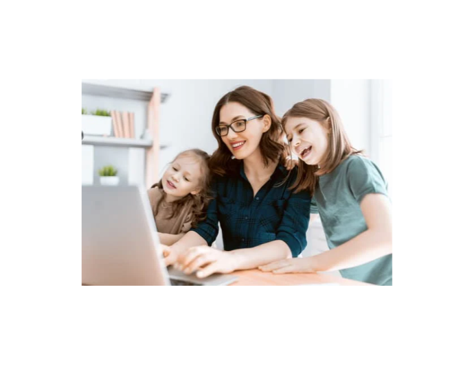 A woman with glasses sitting at a desk with two young girls, all smiling and looking at a laptop together.