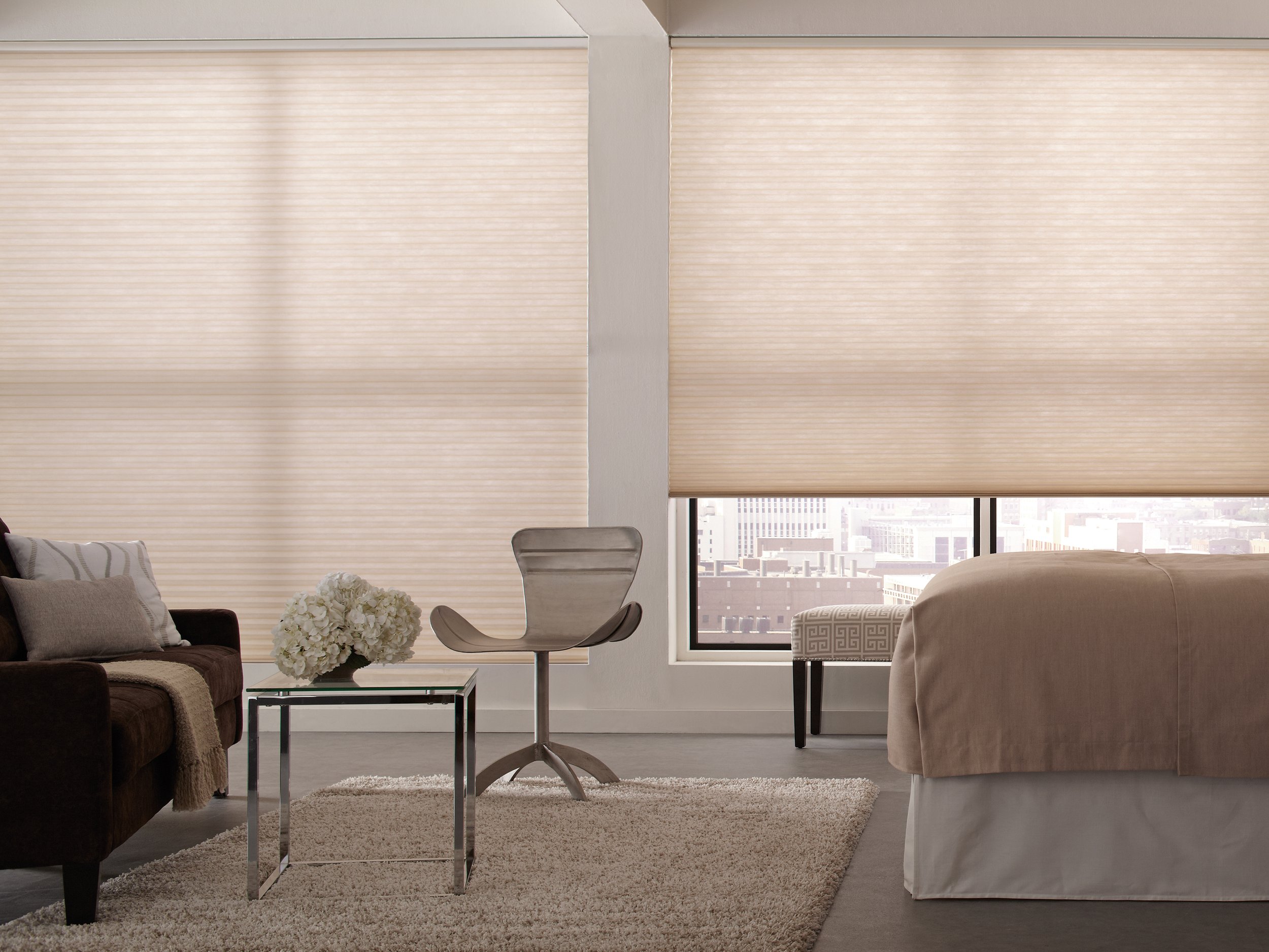 Light-filtering cellular shades in a neutral beige tone covering large windows in a modern bedroom, softly diffusing natural light.