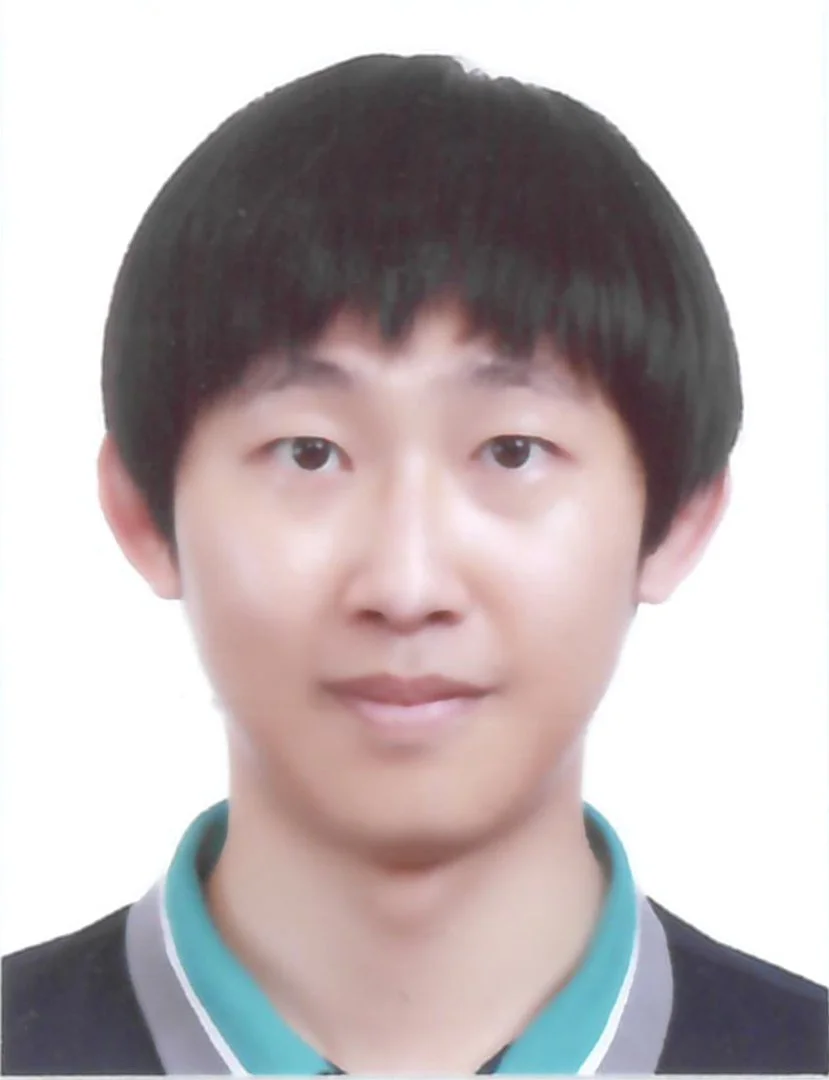 A young Asian man with short black hair, wearing a collared shirt and sweater, smiling slightly against a plain white background.