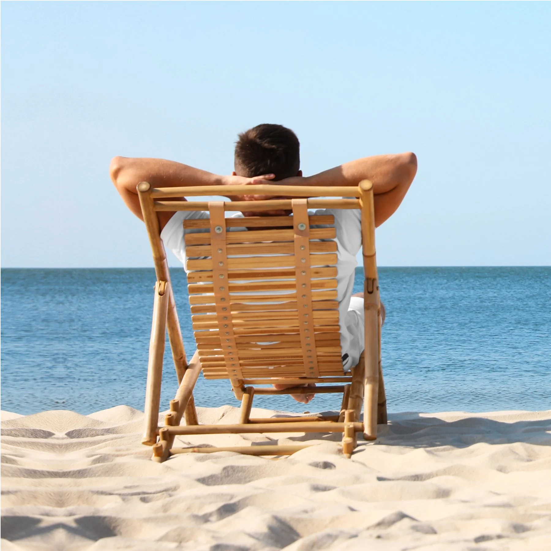 Man relaxing on a wooden beach chair facing the ocean.