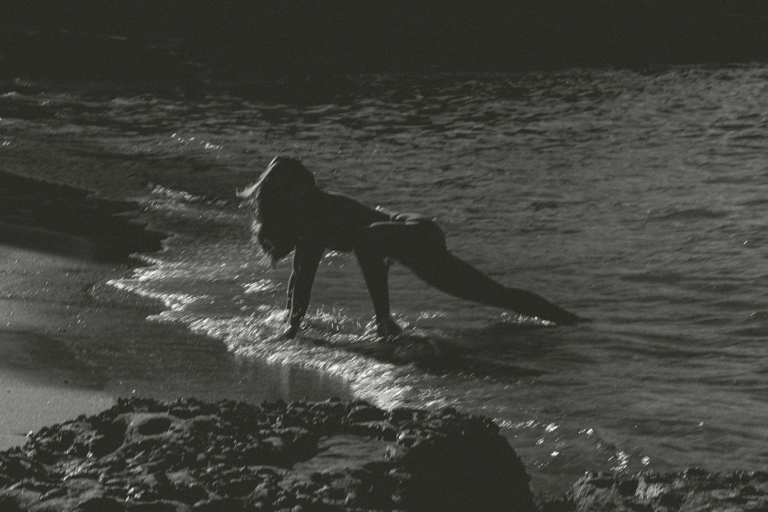 Eine Person beim Sonnenbaden am Strand bei Sonnenuntergang, die auf einem Handtuch sitzt und die Sonne genießt.