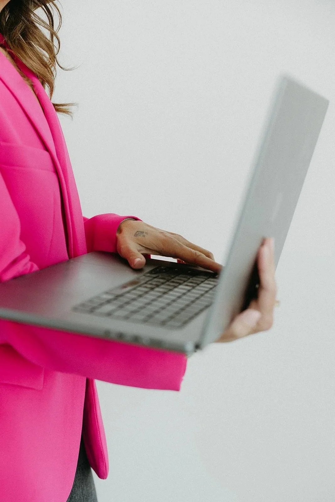 Person in a bright pink blazer using a silver laptop against a plain white background.