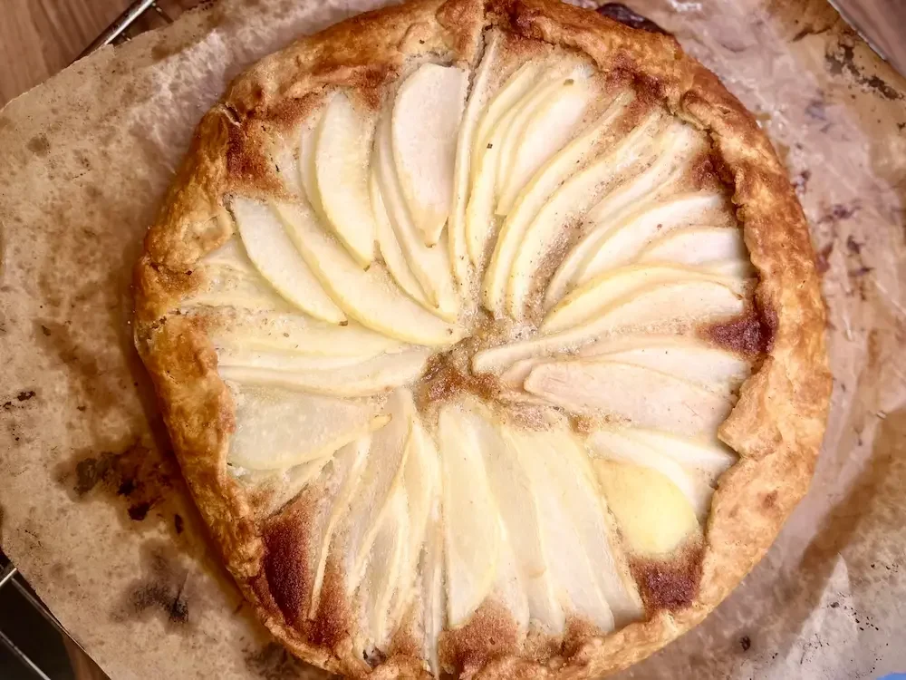 A pear tart with sliced pears arranged in a star pattern on top of a baked crust.