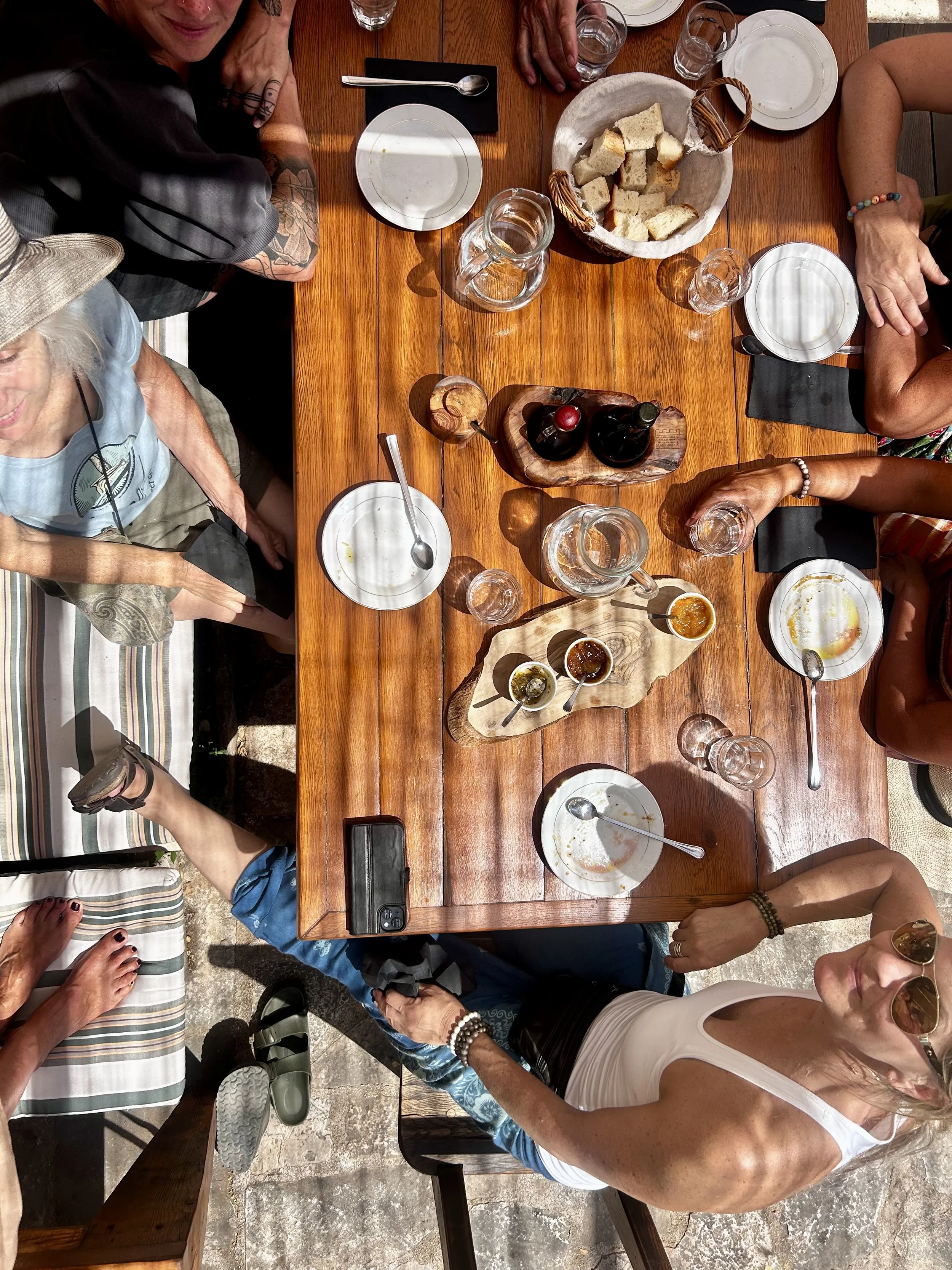 Top-down view of a group of people sitting around a wooden dining table enjoying a meal, with bowls, glasses, condiments, and bread on the table.