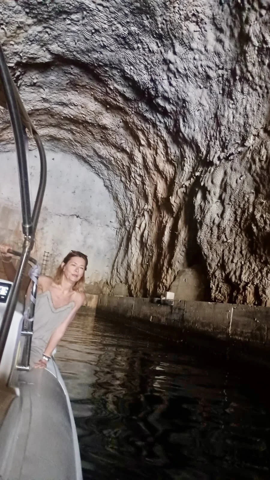 A woman is on a boat in an underground water cavern with rugged rock walls and pool of water.