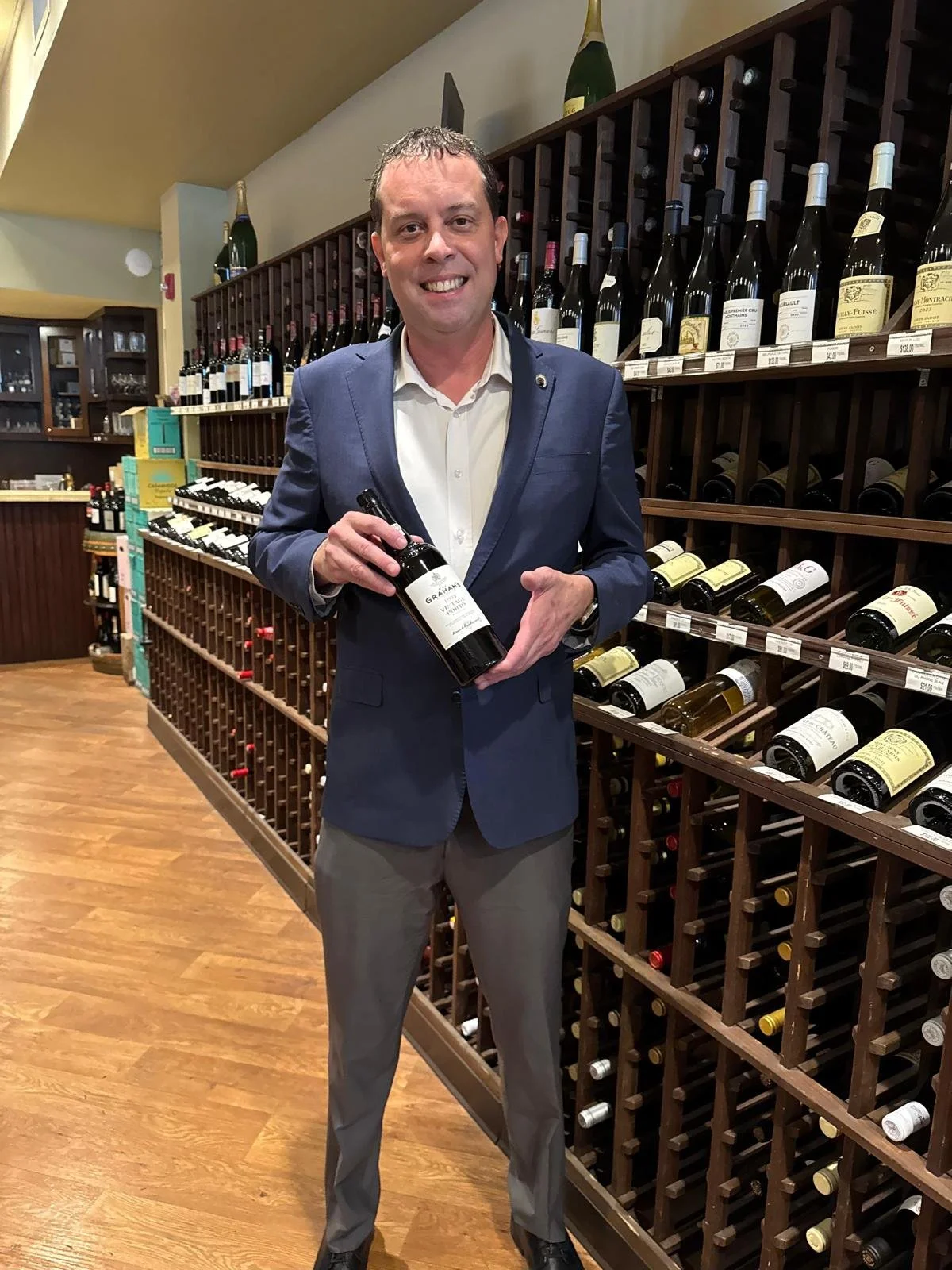 A modern building with wood and stone exterior on a grassy hillside, with a backdrop of snow-capped mountains under a cloudy sky.