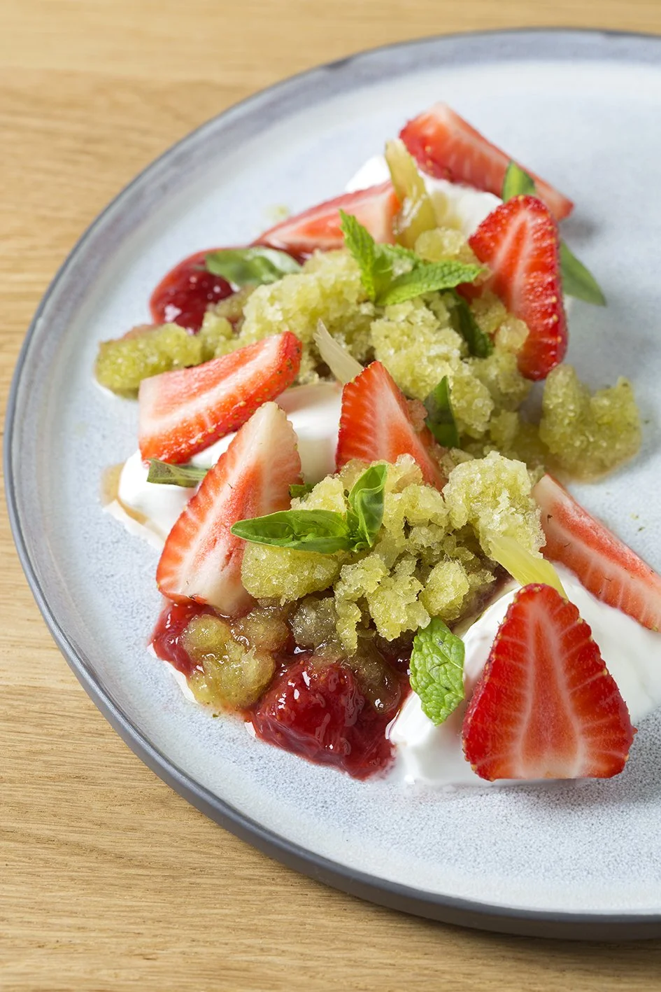 Postre de frutillas, crema, y menta en plato blanco
