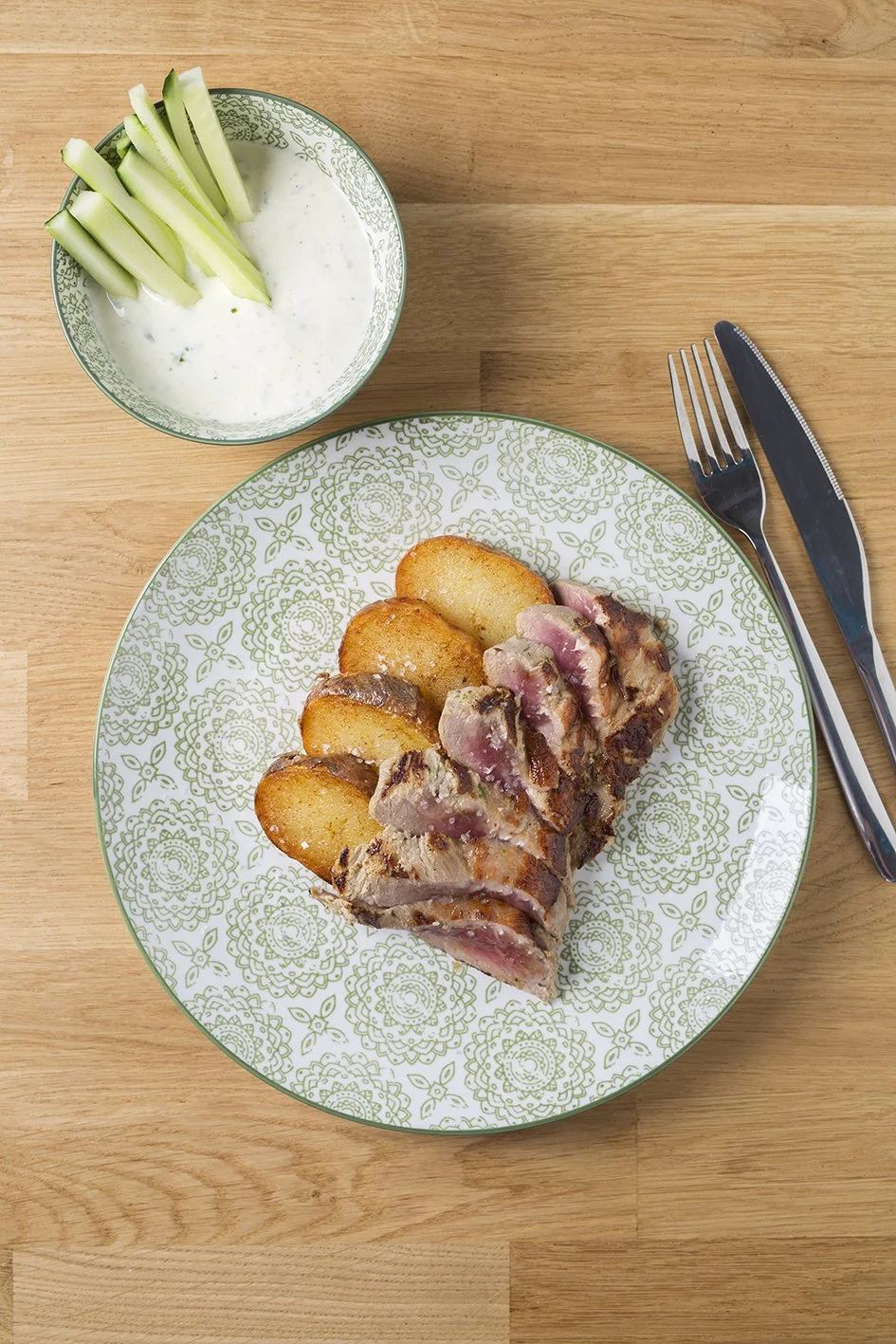 Plato con filete de pescado y papas fritas, acompañado de salsa de yogurt con apio, todo sobre una mesa de madera.