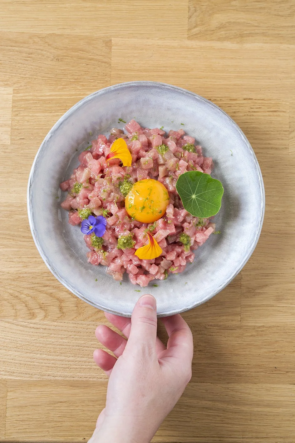 Tartar de carne con un huevo crudo en el centro decorado con flores comestibles y una hoja.
