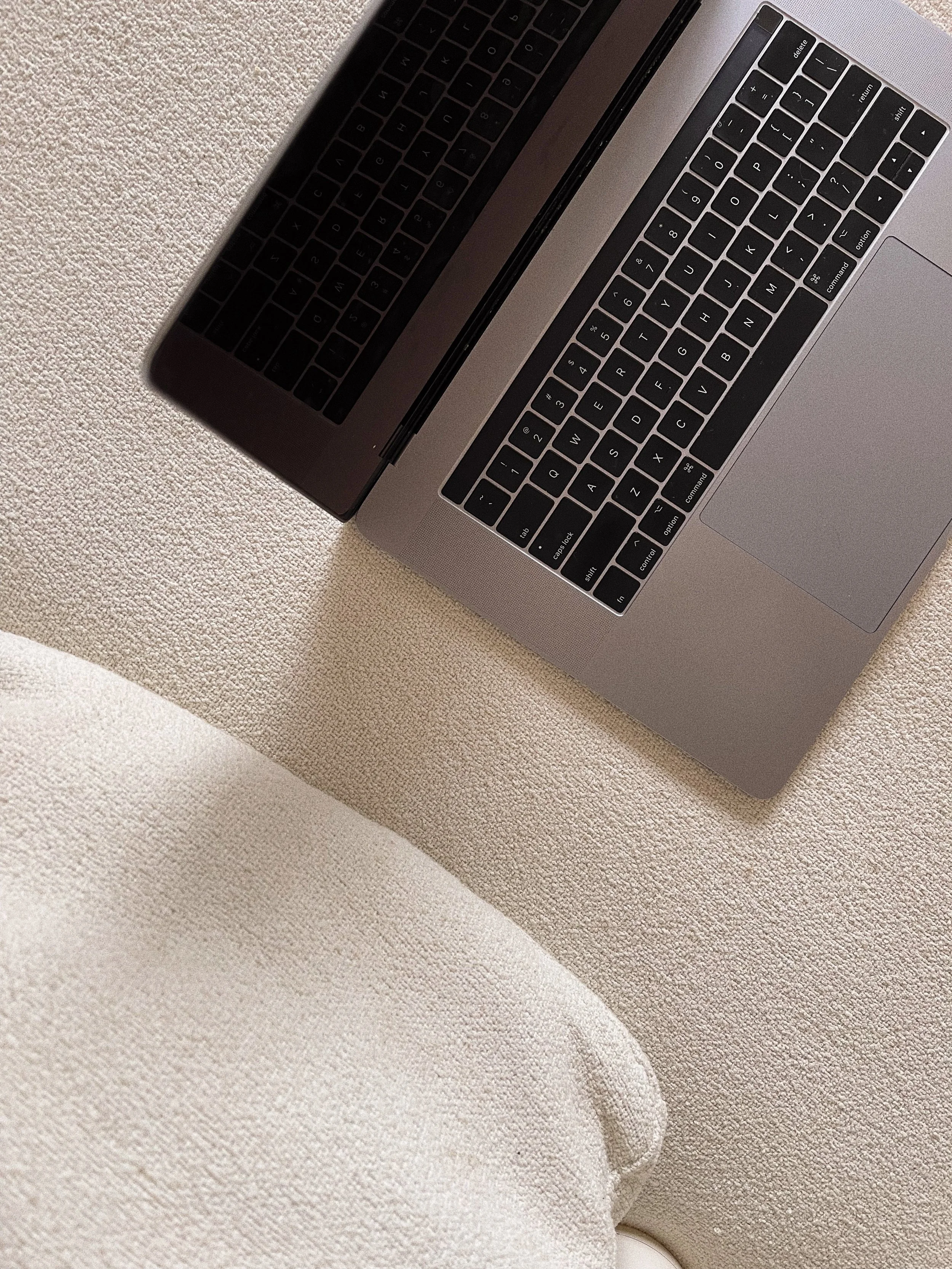 Close-up of a silver laptop with a black keyboard, resting on a beige textured surface and a white fabric item nearby. Shows the work-life balance of a digital nomad and online content creator with a DIY website.