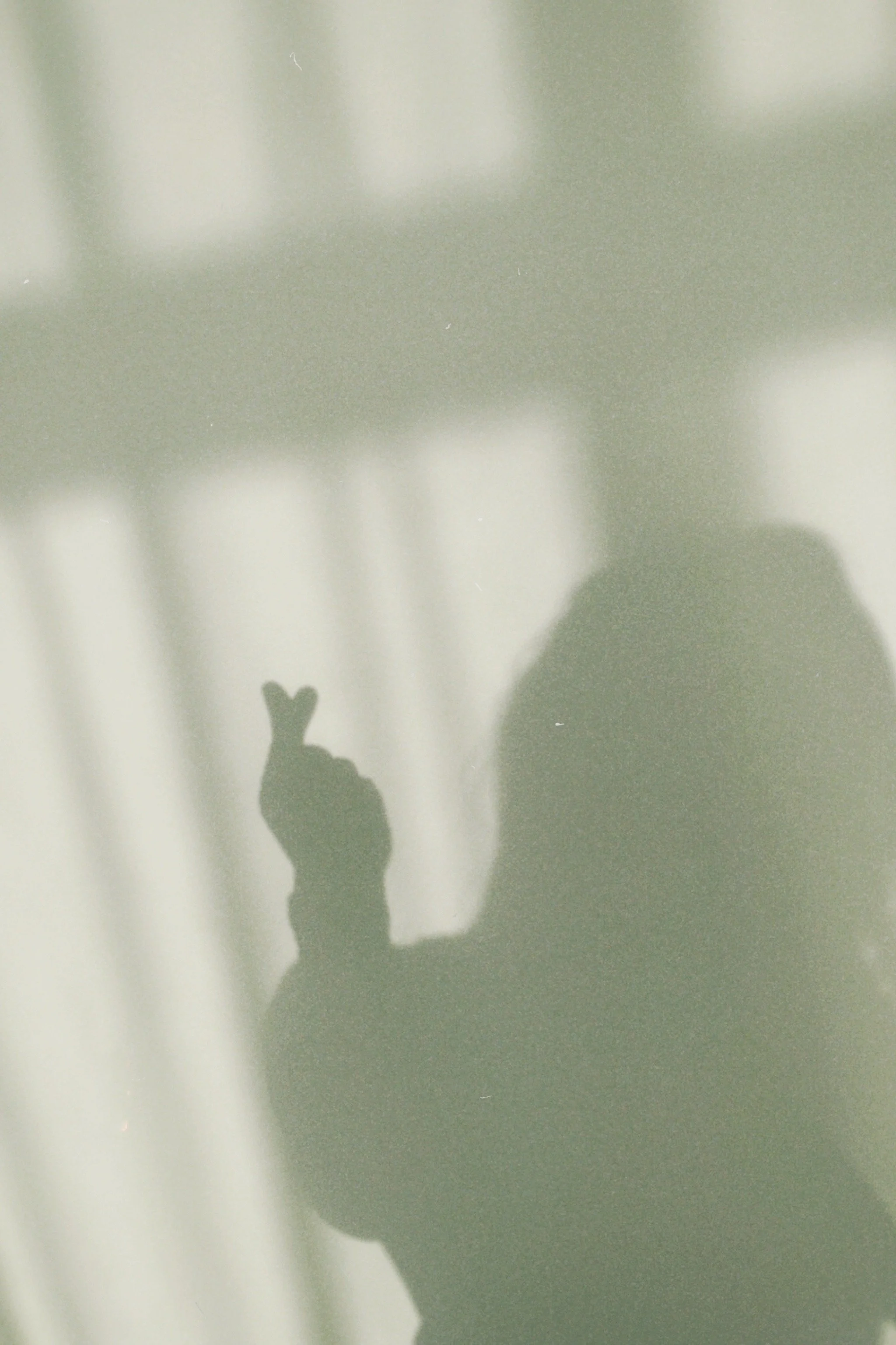 Shadow of a person making a peace sign with their hand, cast on a light-colored curtain or window blind.
