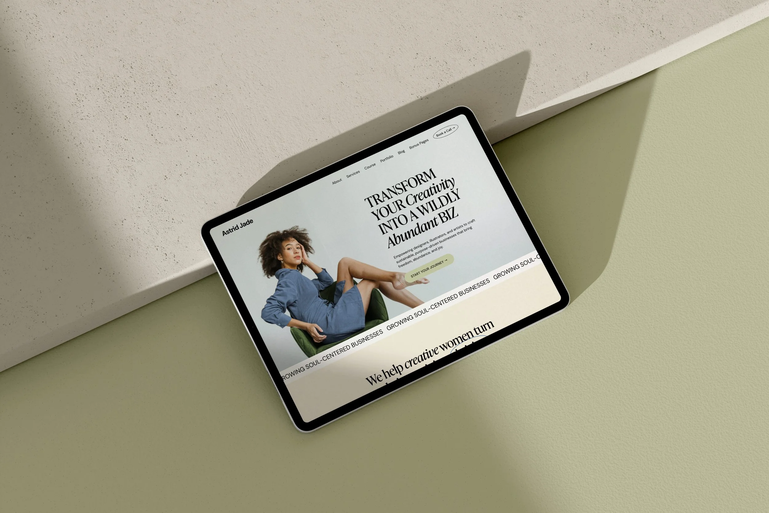 Tablet displaying a website with a woman in a blue dress sitting on a green chair, with text about transforming creativity into a business.