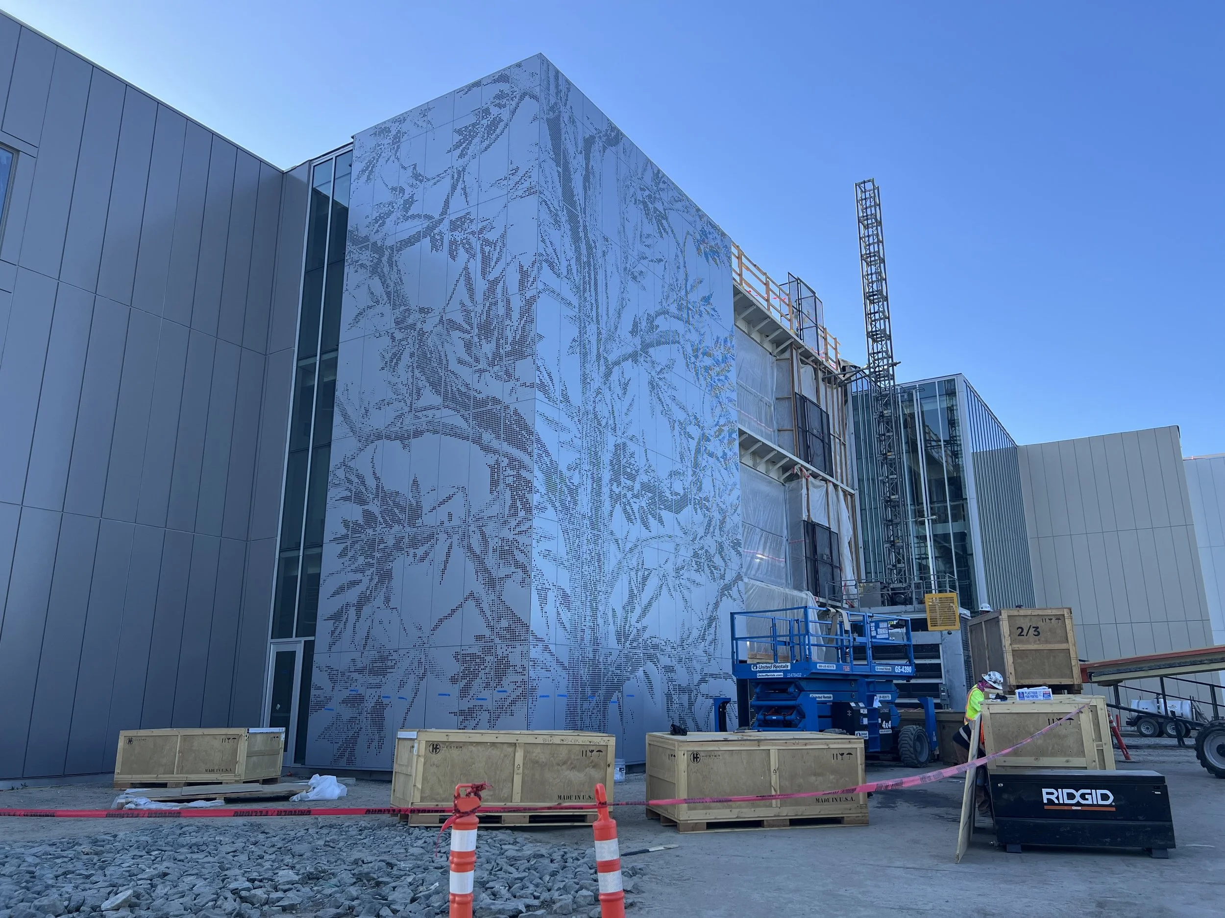 Construction site of a modern building with a large decorative metal panel featuring a bamboo design on the exterior wall, construction equipment, and workers.