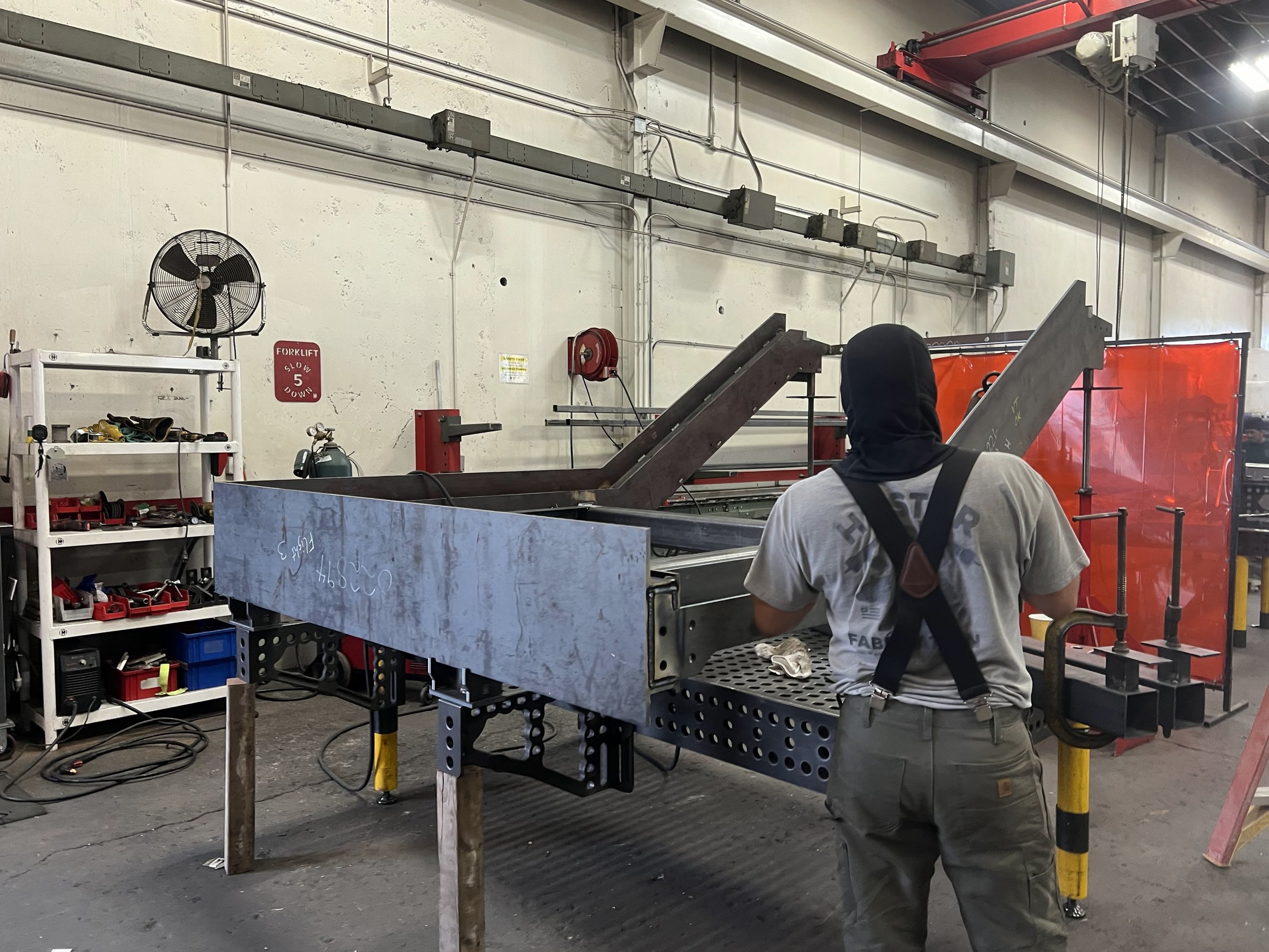 A person working on a metal construction in a workshop with tools and equipment around.