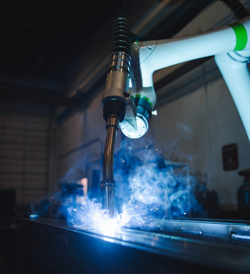 A robotic welding arm performing automated welding on a metal surface with sparks and smoke.