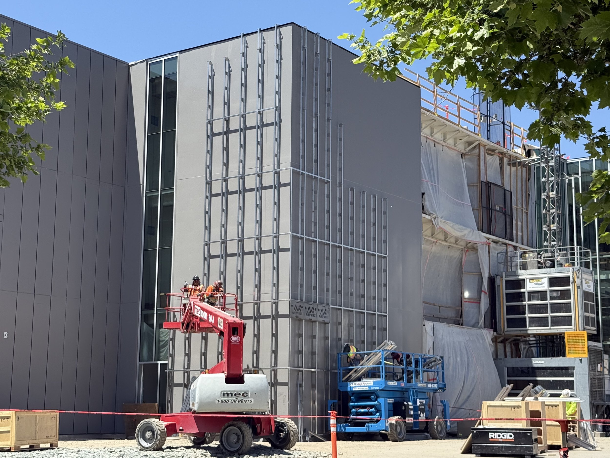 Construction workers on a cherry picker working on the exterior of a modern building under construction with scaffolding and construction equipment around.