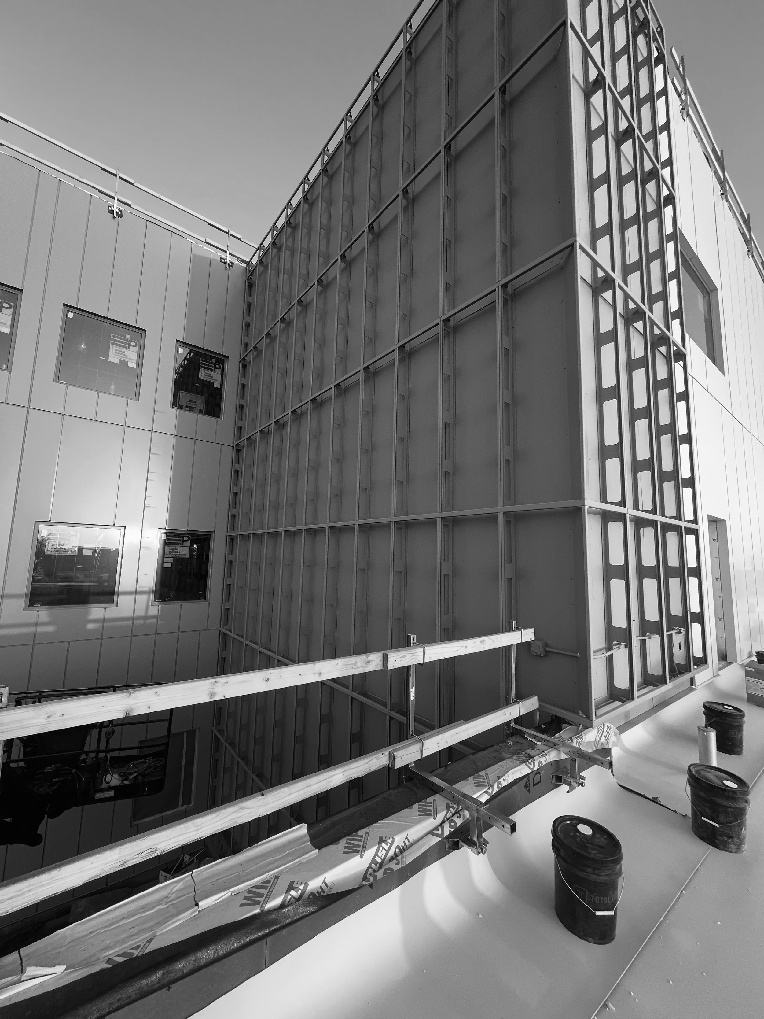 Construction site of a modern building with metal walls, scaffolding, and buckets of materials on the roof.