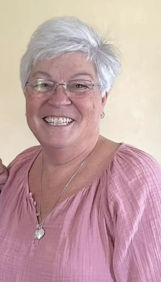 Scenic landscape of mountains, a lake, and rolling hills with sparse trees, under cloudy sky.