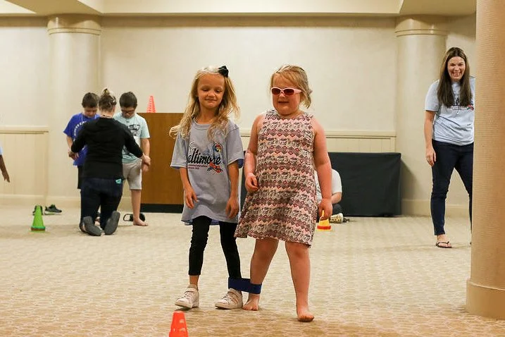 Two girls standing side by side with their inner legs band together in a 3-legged race.