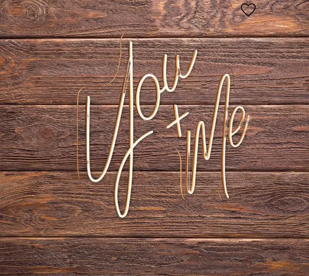 Neon sign on wood background that says "You + Me" with a small heart at the top right corner.