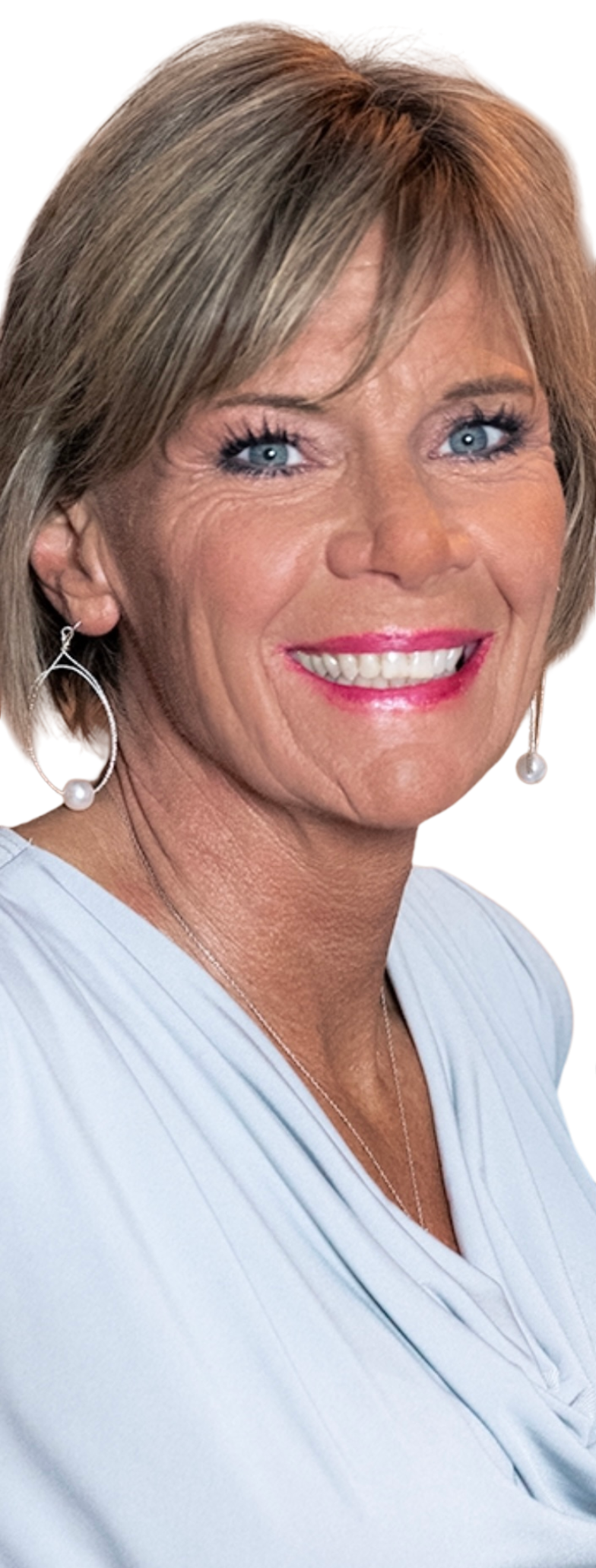A smiling woman with short blond hair, blue eyes, and pearl earrings, wearing a light blue top.
